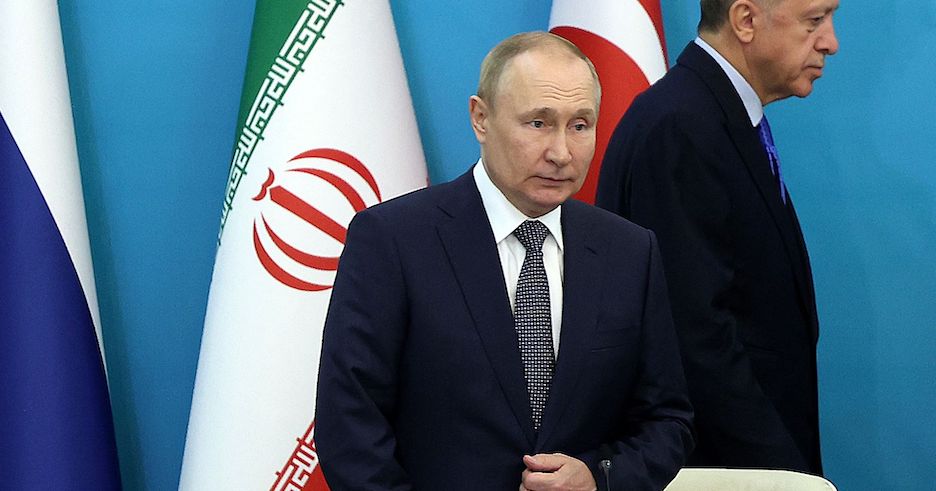 Wladimir Putin vor der russischen, iranischen und türkischen Fahne. Er wirkt überrascht und angeschlagen. Hinter seinem Rücken geht der türkische Präsident Erdogan vorbei.