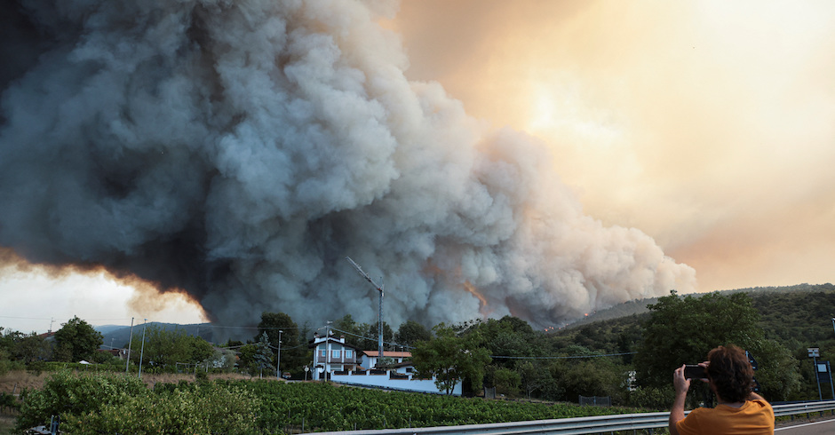 Eine gigantisch Rauchsäule steigt hinter einem Hügel auf und verdeckt die Sonne. Ein Mann fotografiert das Spektakel