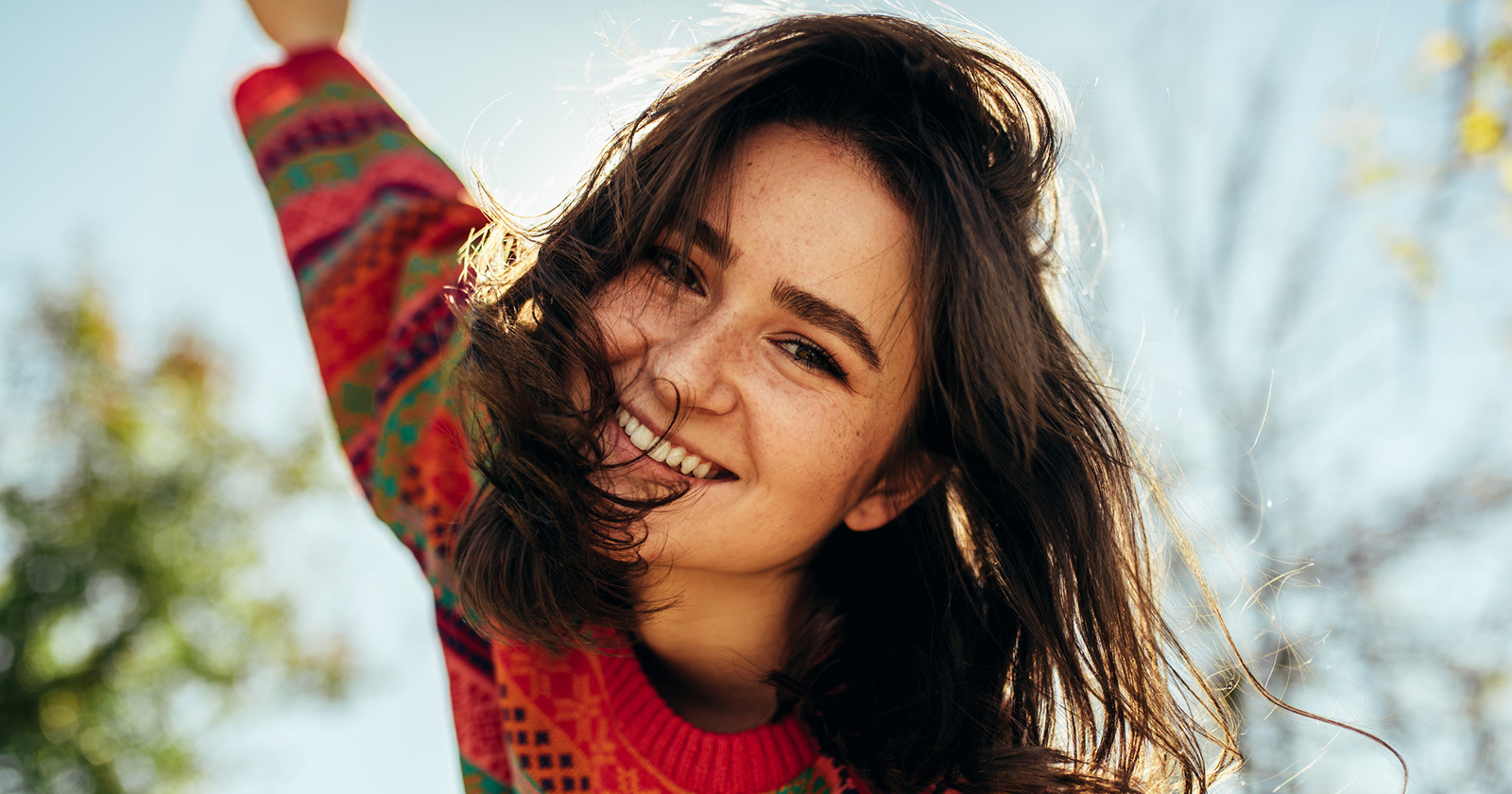 Junge fröhliche Frau beim Spazierengehen an einem sonnigen Herbstnachmittag | Credit: iStock.com/Yuricazac