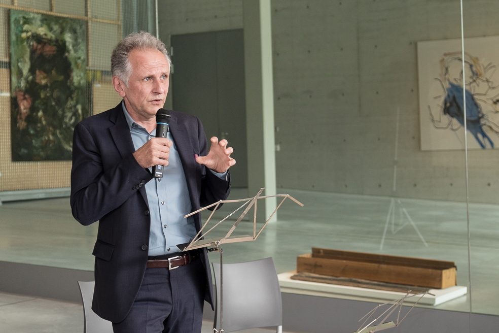 Mann moderiert vor einem Kunstobjekt