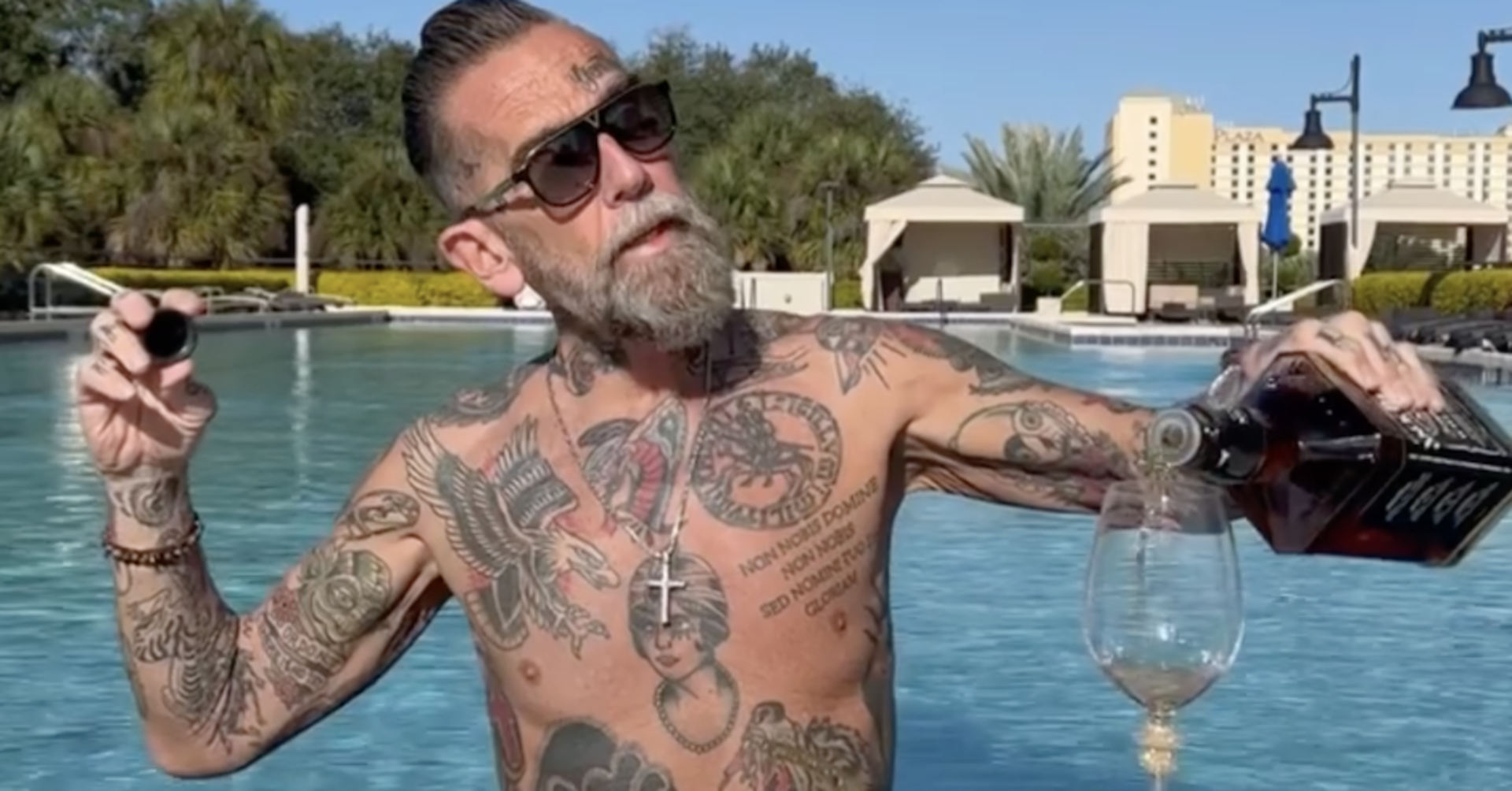 Roland Ludomirska mit nackten Oberkörper, voll tättowiert und einer Flasche Jack Daniels in einem Pool