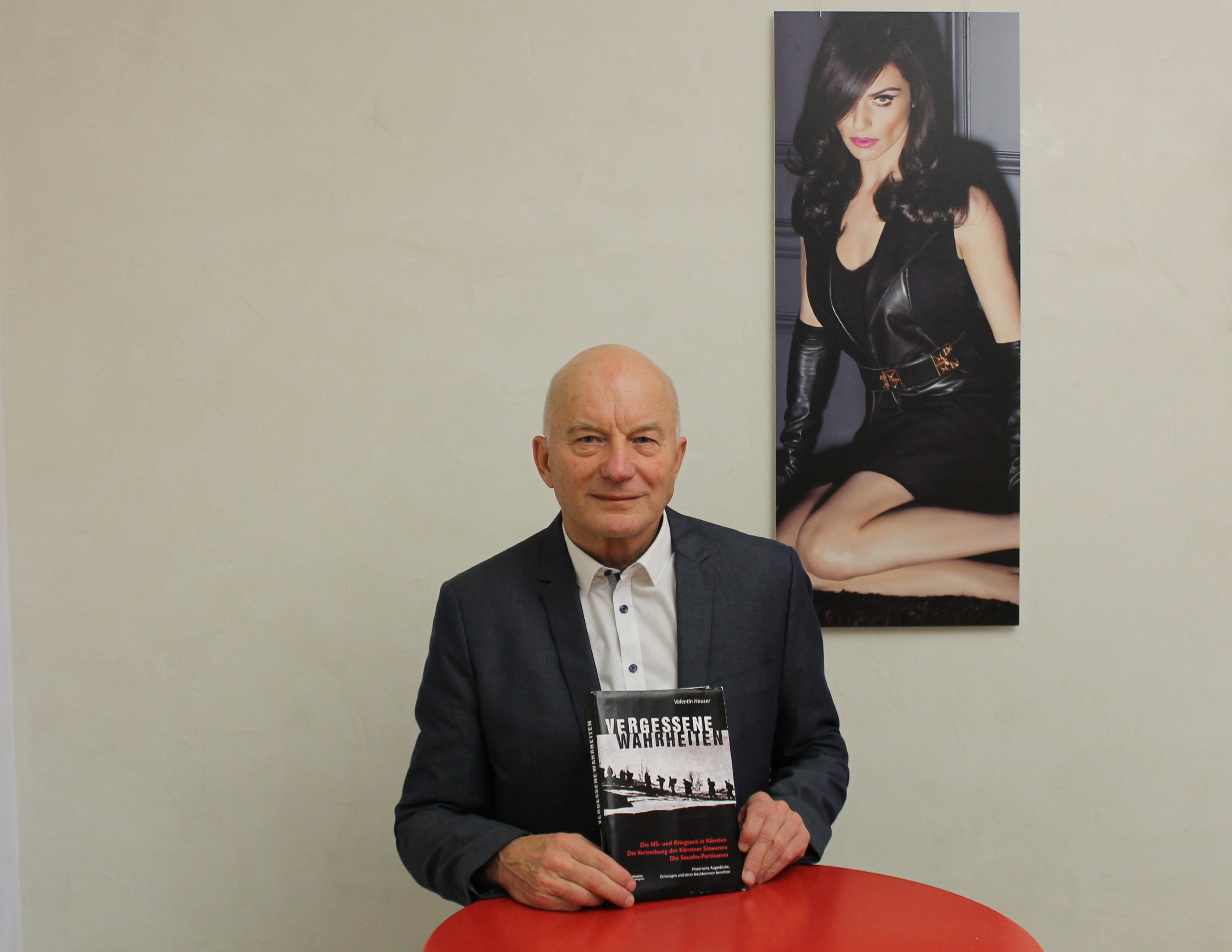 Valentin Hauser steht in einen Anzug gekleidet und mit seinem neuen Buch in der Hand hinter einem roten Stehtisch