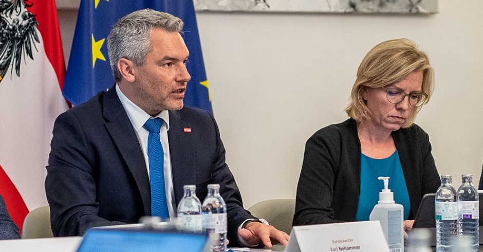 Bundeskanzler Karl Nehammer (ÖVP) und Klimaschutzministerin Leonore Gewessler (Grüne) vor der österreichischen und europäischen Flagge beim Energiegipfel. Sie sitzen nebenbeinander, Nehammer spricht. Aufnahem aus dem Gespräch