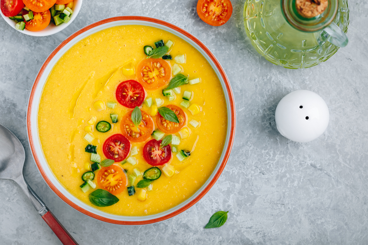 Eine Schüssel mit Mais-Gazpacho sowie einer Garnitur aus Tomaten und Gewürzen