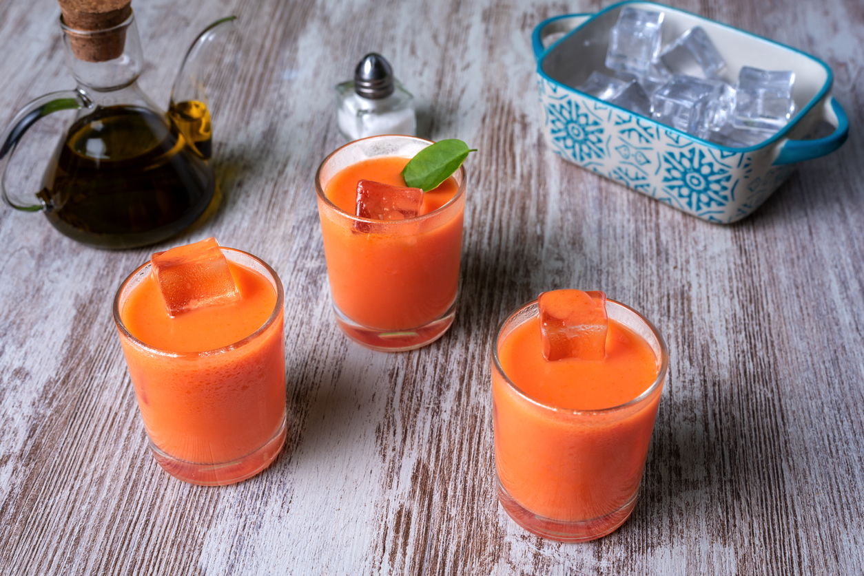 Drei Shotgläser mit Gazpacho und Eiswürfeln gefüllt