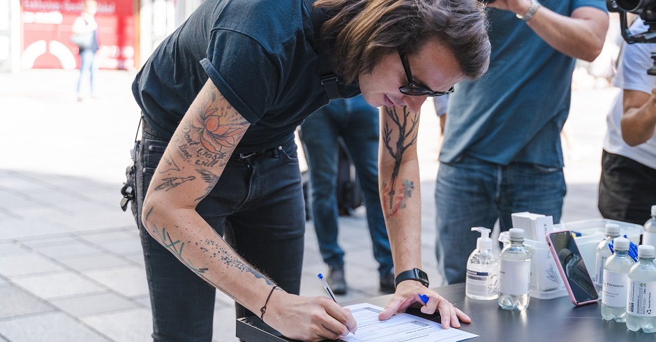 Pogo mit T-Shirt, Gillet, Sonnenbrille und Tattoos beim Unterschreiben der Unterstützungserklärung.