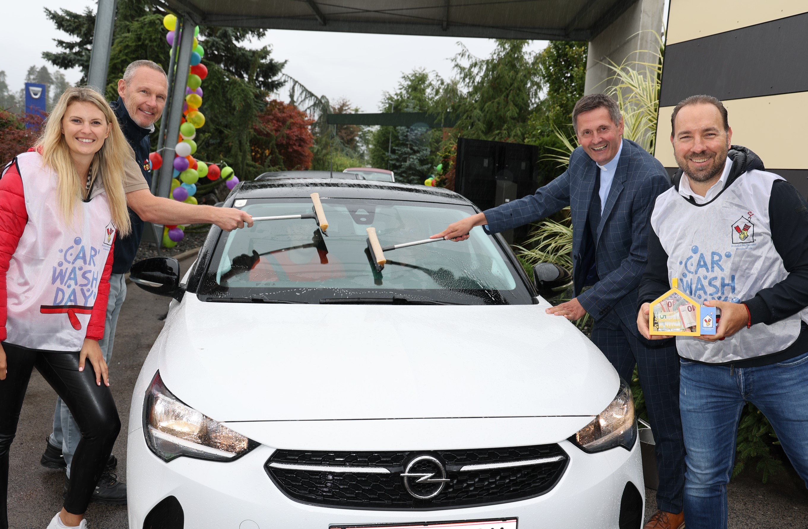 Vier Personen putzen die Scheibe eines Autos