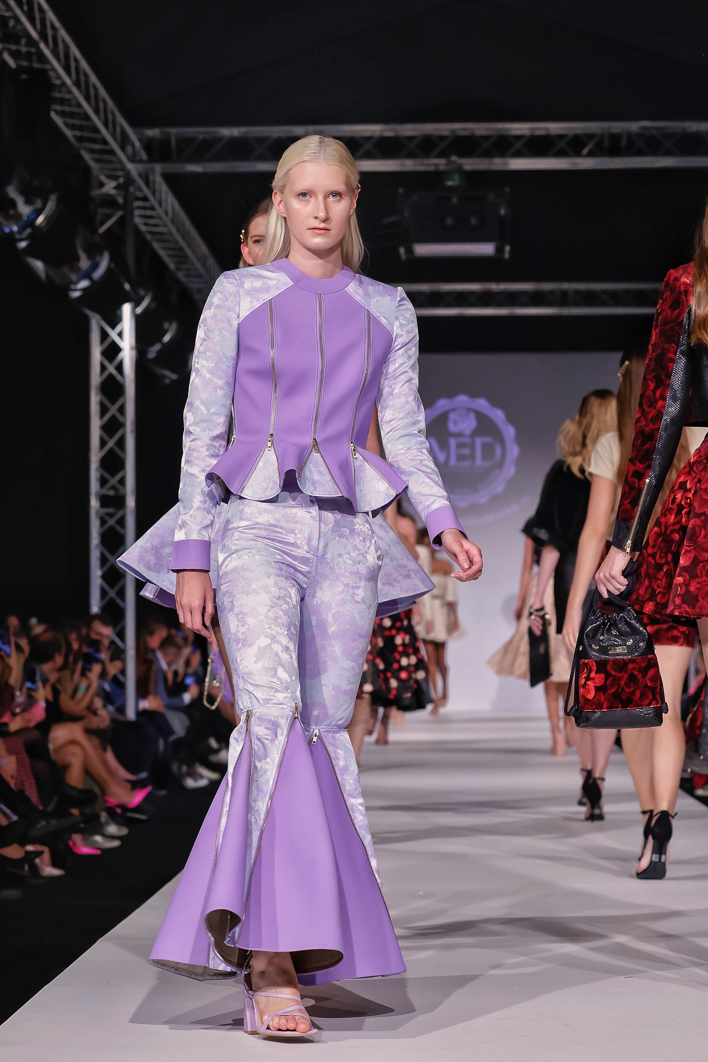 Model in einer fliederfarbenen Kombi am Laufsteg