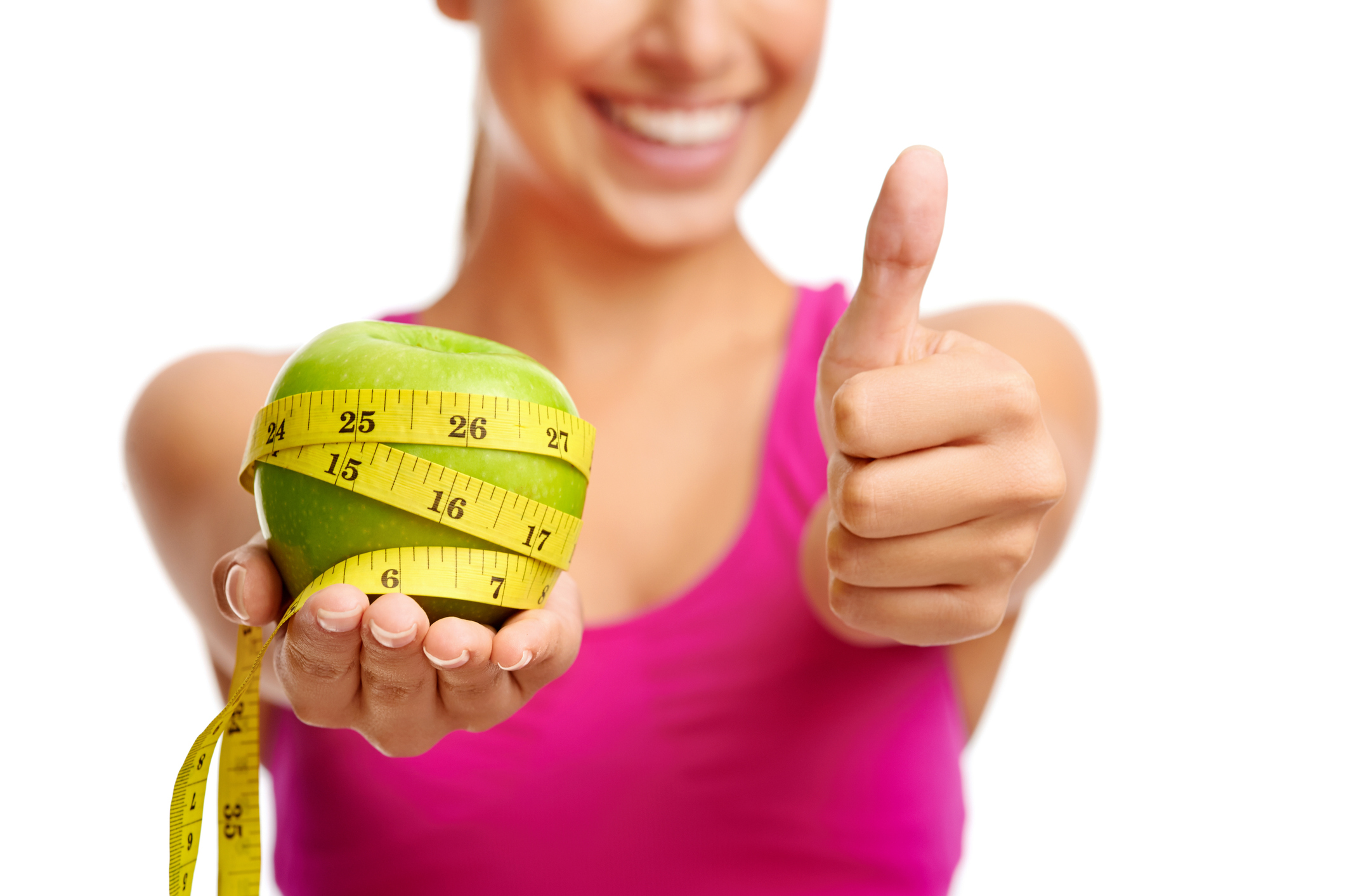 Eine junge schlanke Frau, die einen Apfel in der Hand hält, der mit einem Maßband umwickelt ist, und eine Daumenhoch-Geste vollführt