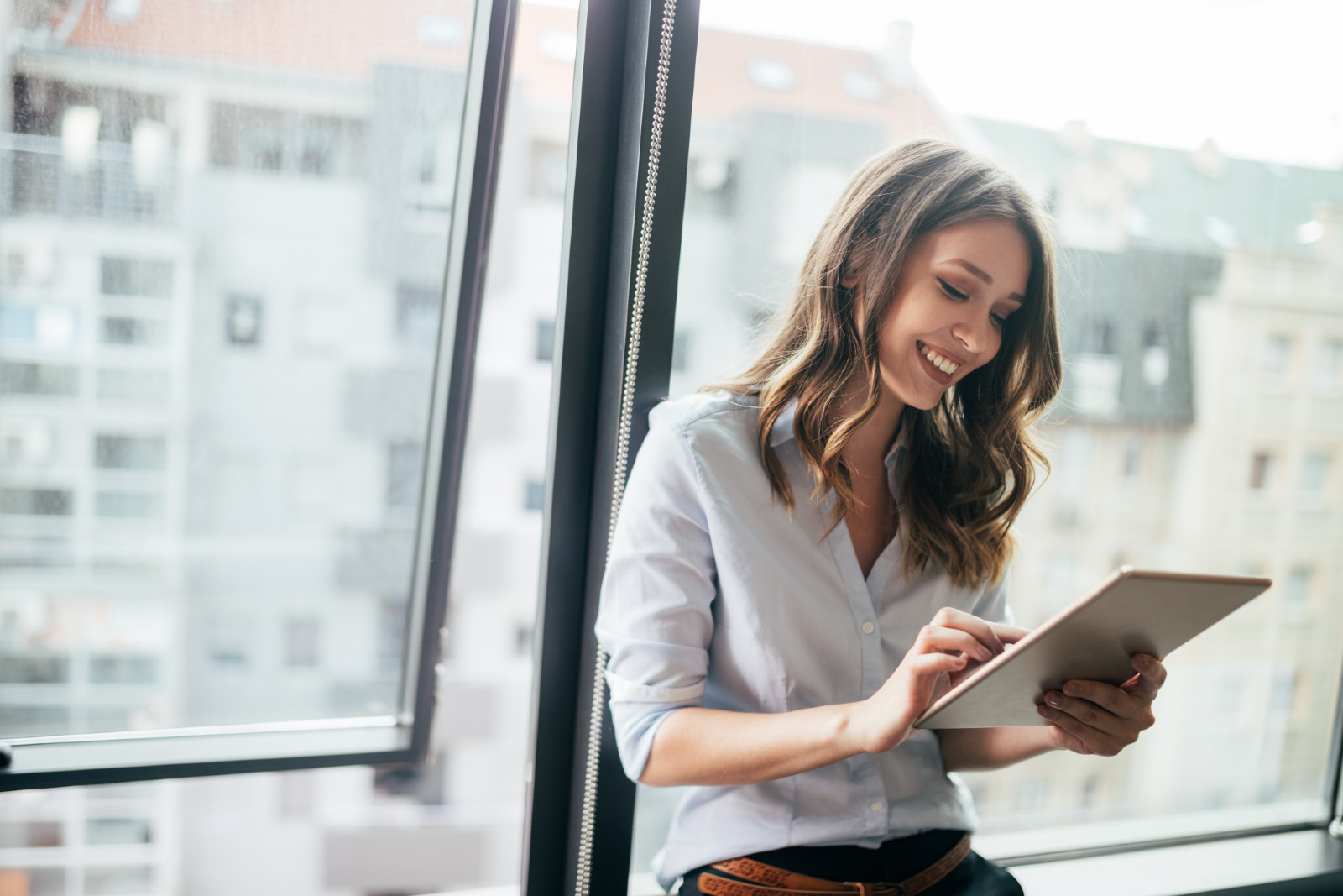 Frau steht lächelnd mit Tablet in der Hand am Fenster | Credit: iStock.com/nd3000