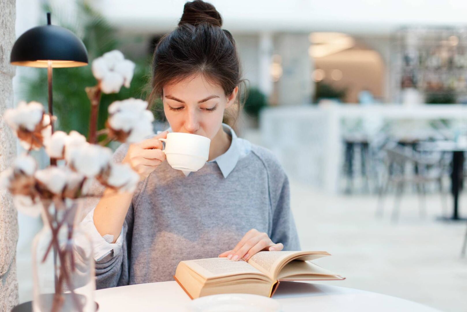 Junge Lokalbesucherin beim Lesen mit einer Tasse Kaffee in der Hand | Credit: iStock.com/Maryna Andriichenko