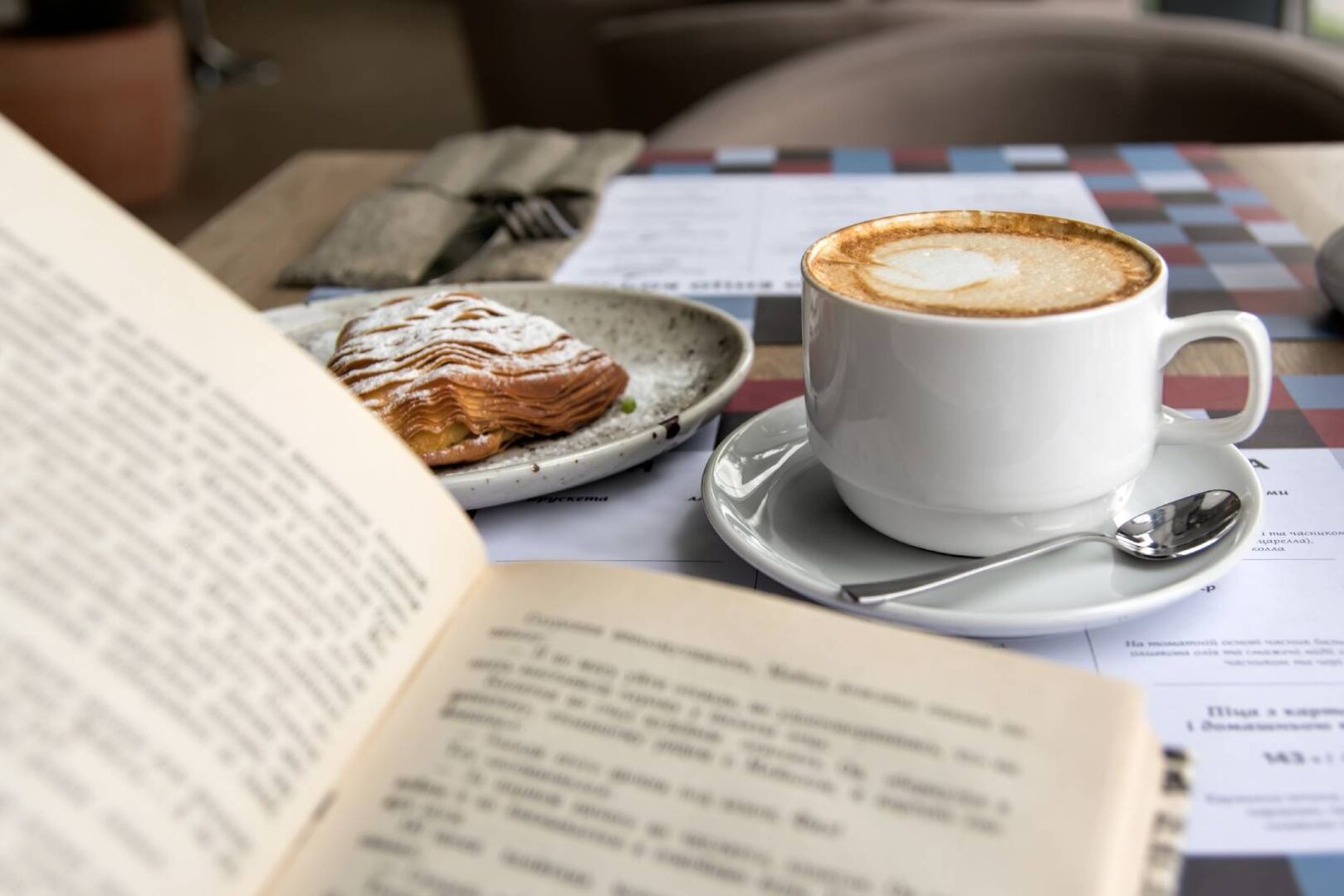 Offene Buch und Tasse Café auf einem Tisch in einem Lokal | Credit: iStock.com/taratata
