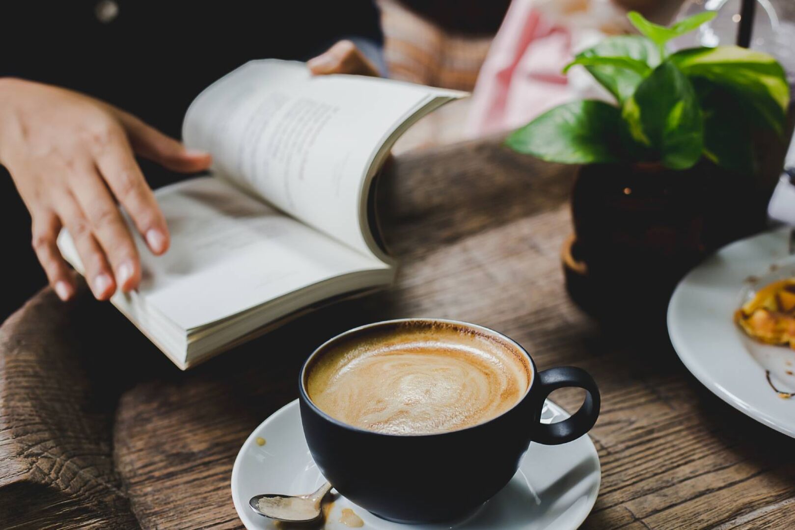 Junge Frau beim Lesen im Café mit einer Tasse Cappuccino in Reichweite | Credit: iStock.com/TK 1993