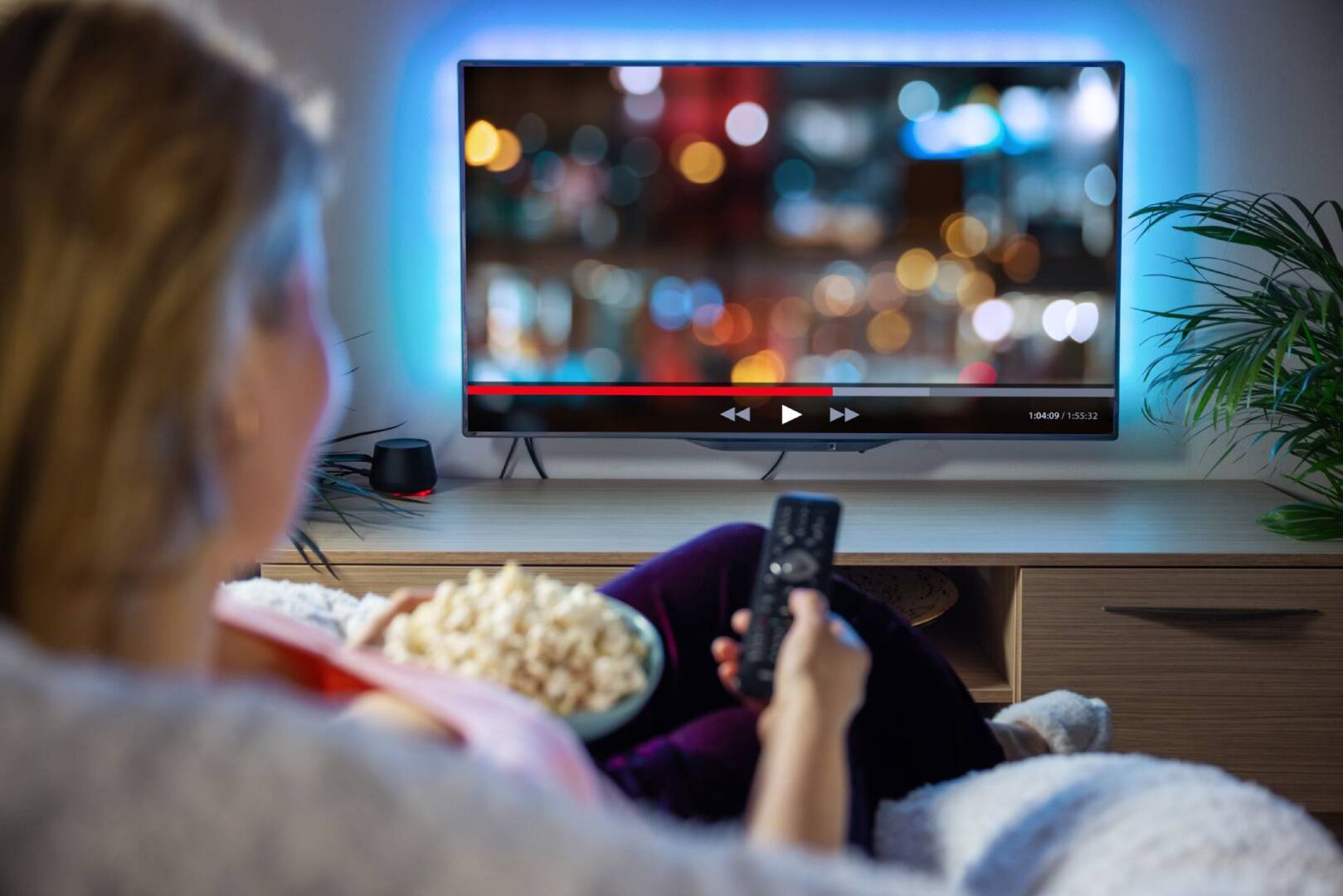 Junge Frau beim Fernsehen mit einer Schale Popcorn in der Hand | Credit: iStock.com/grinvalds