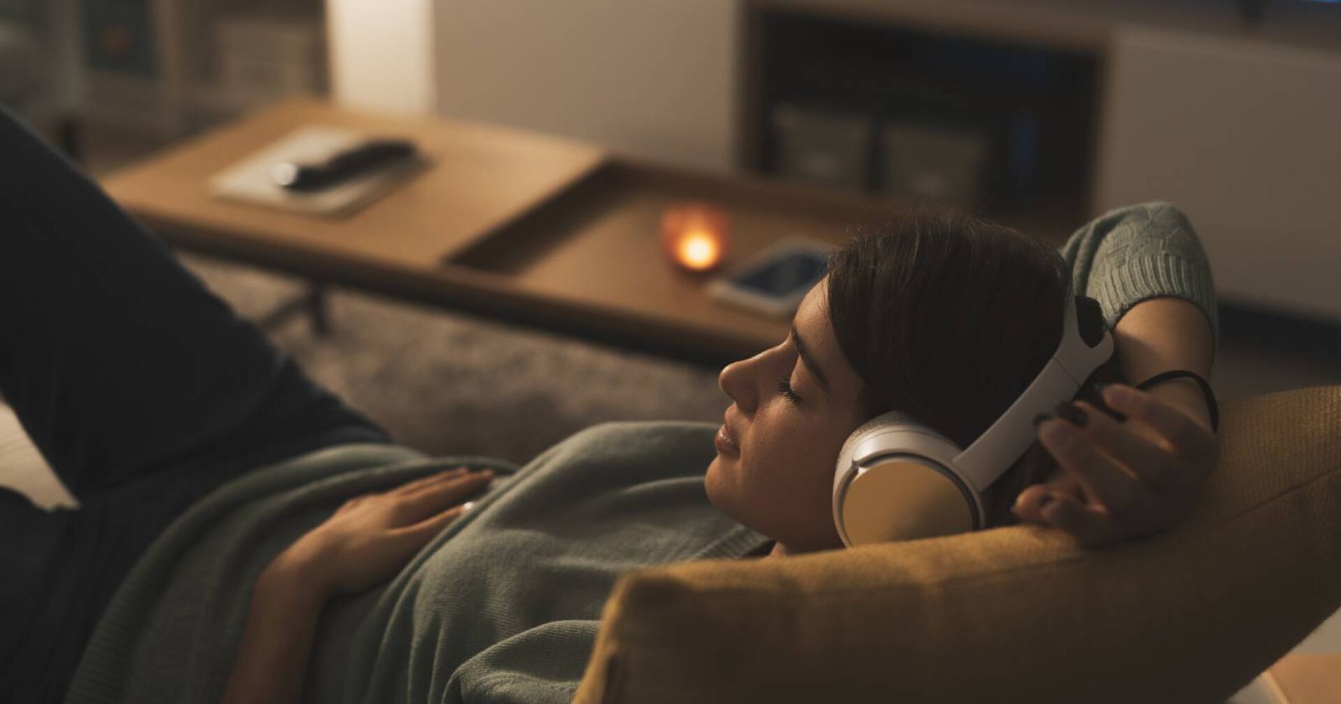 Junge Frau auf ihrer Couch beim entspannten Musikhören | Credit: iStock.com/cyano66