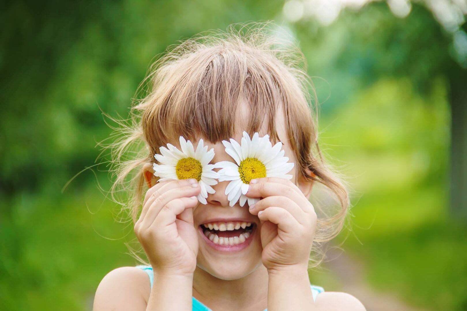 Fröhliches Mädchen mit Margeritenblüten vor den Augen | Credit: iStock.com/Yana Tatevosian