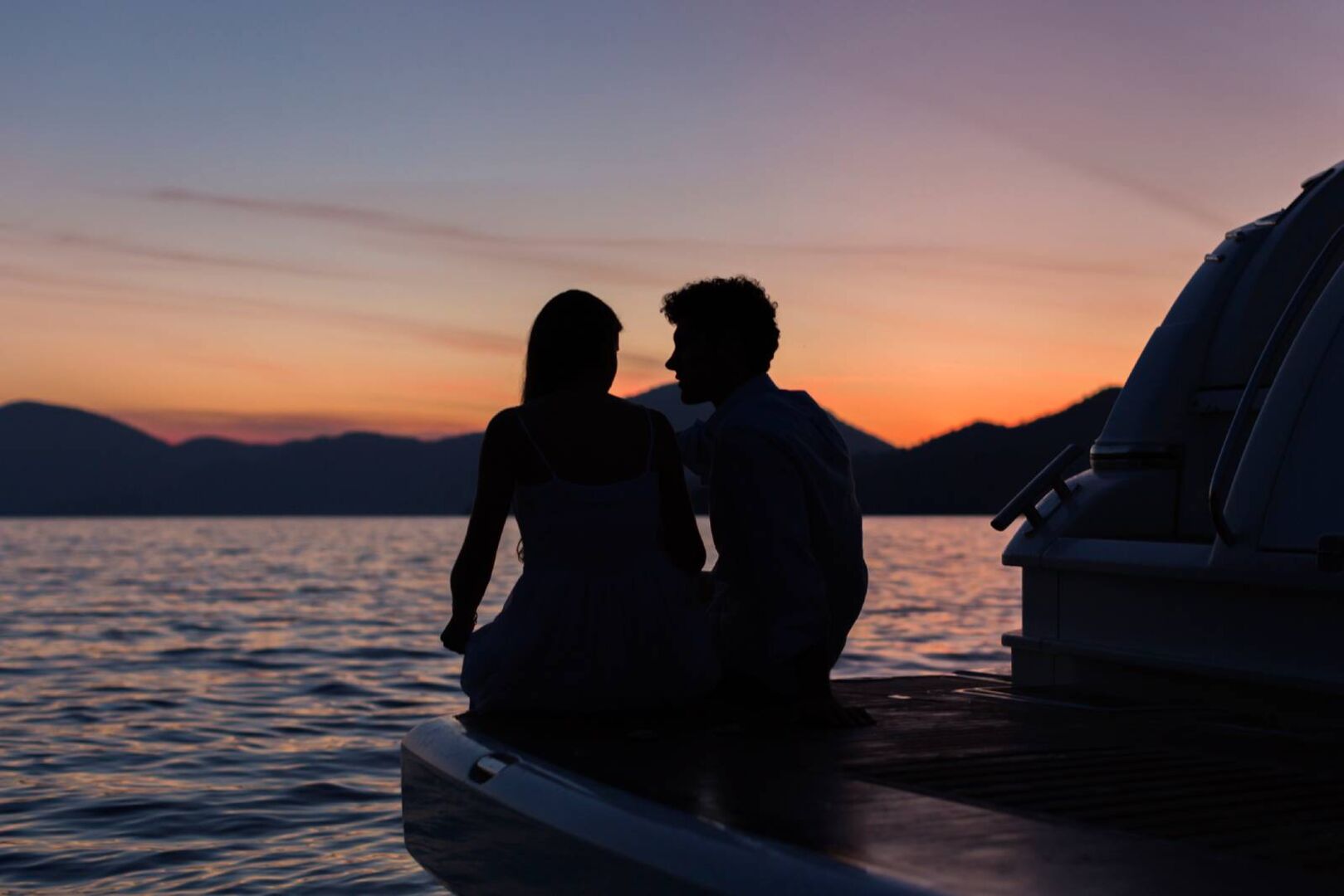 Junges verliebtes Paar im Sonnenuntergang am Ufer eines Sees | Credit: iStock.com/Dreamer Company