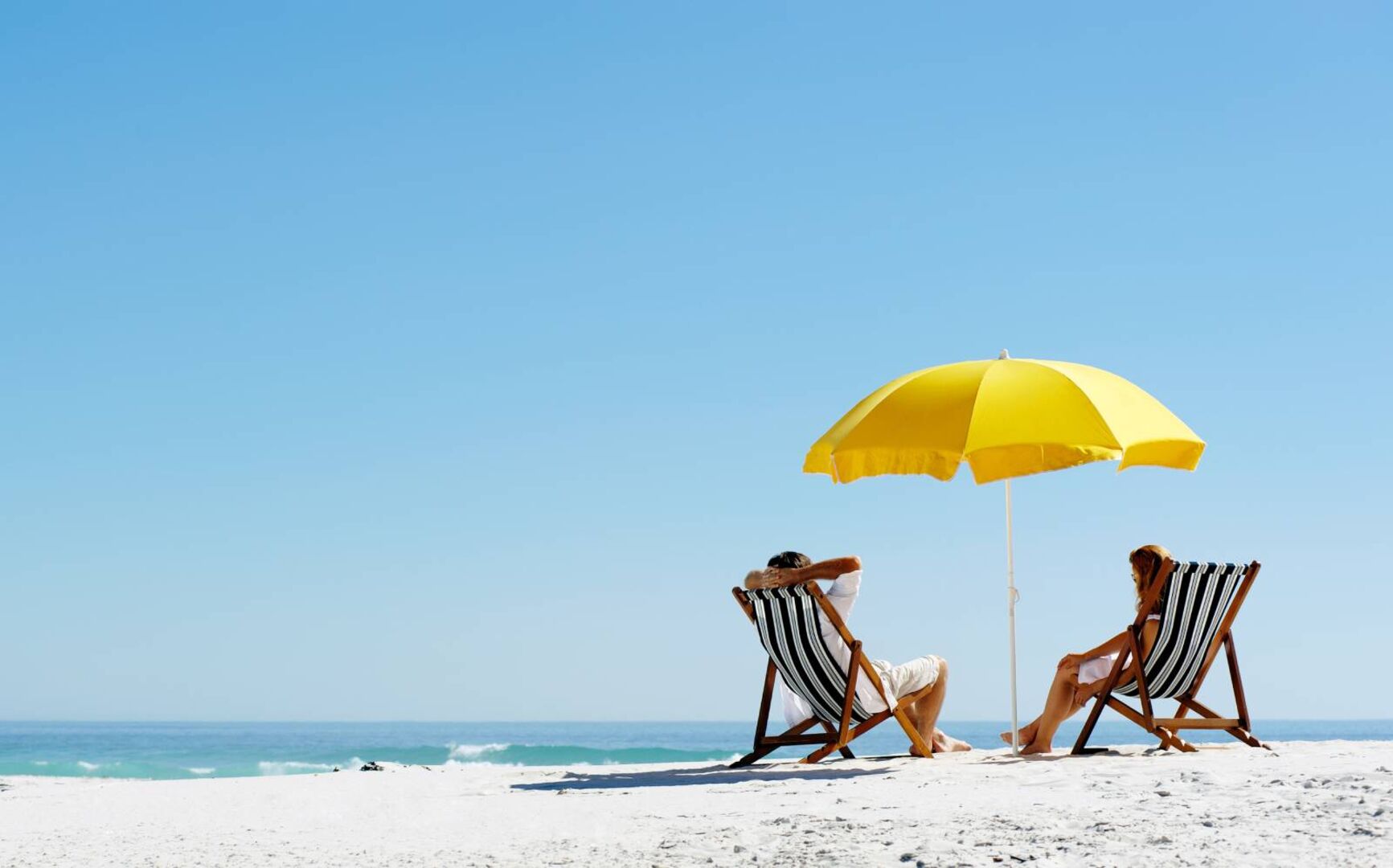 Paar im Liegestuhl unterm Sonnenschirm am Strand | Credit: iStock.com/warrengoldswain