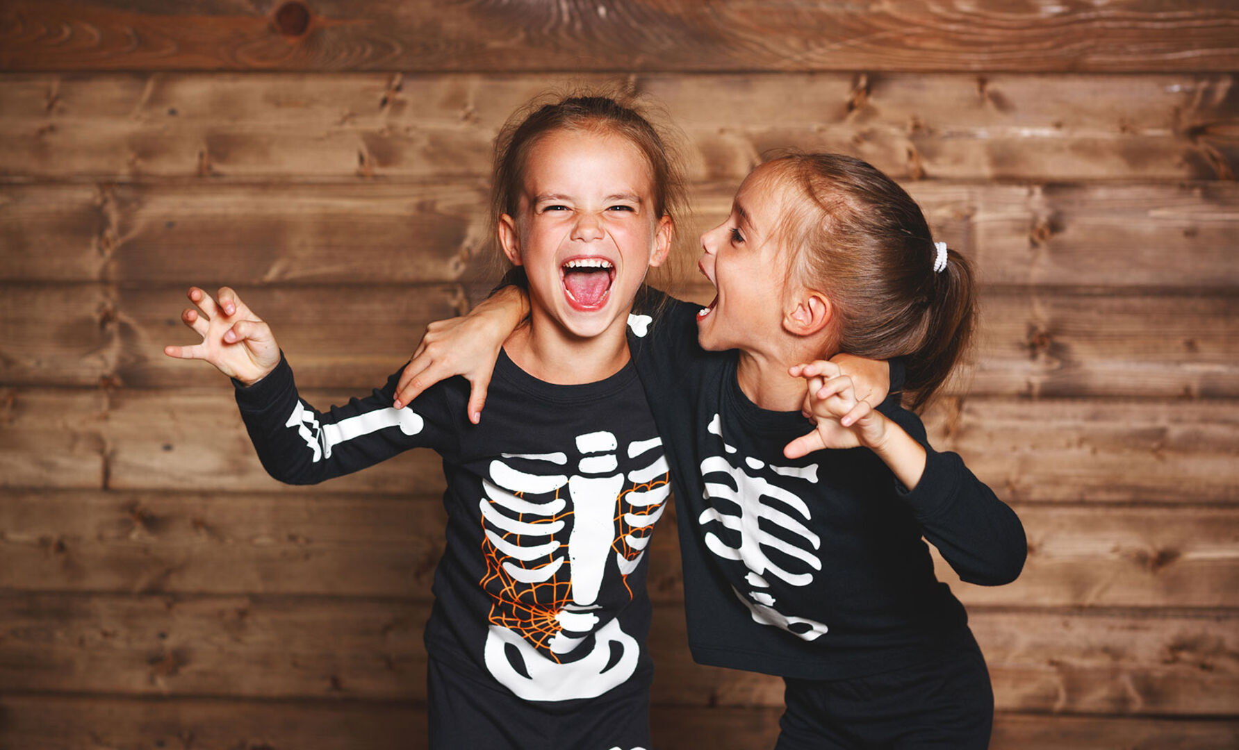 Zwei kleine Mädchen mit schwarzen Skelett-Shirts im Rahmen von Halloween | Credit: iStock.com/evgenyatamanenko