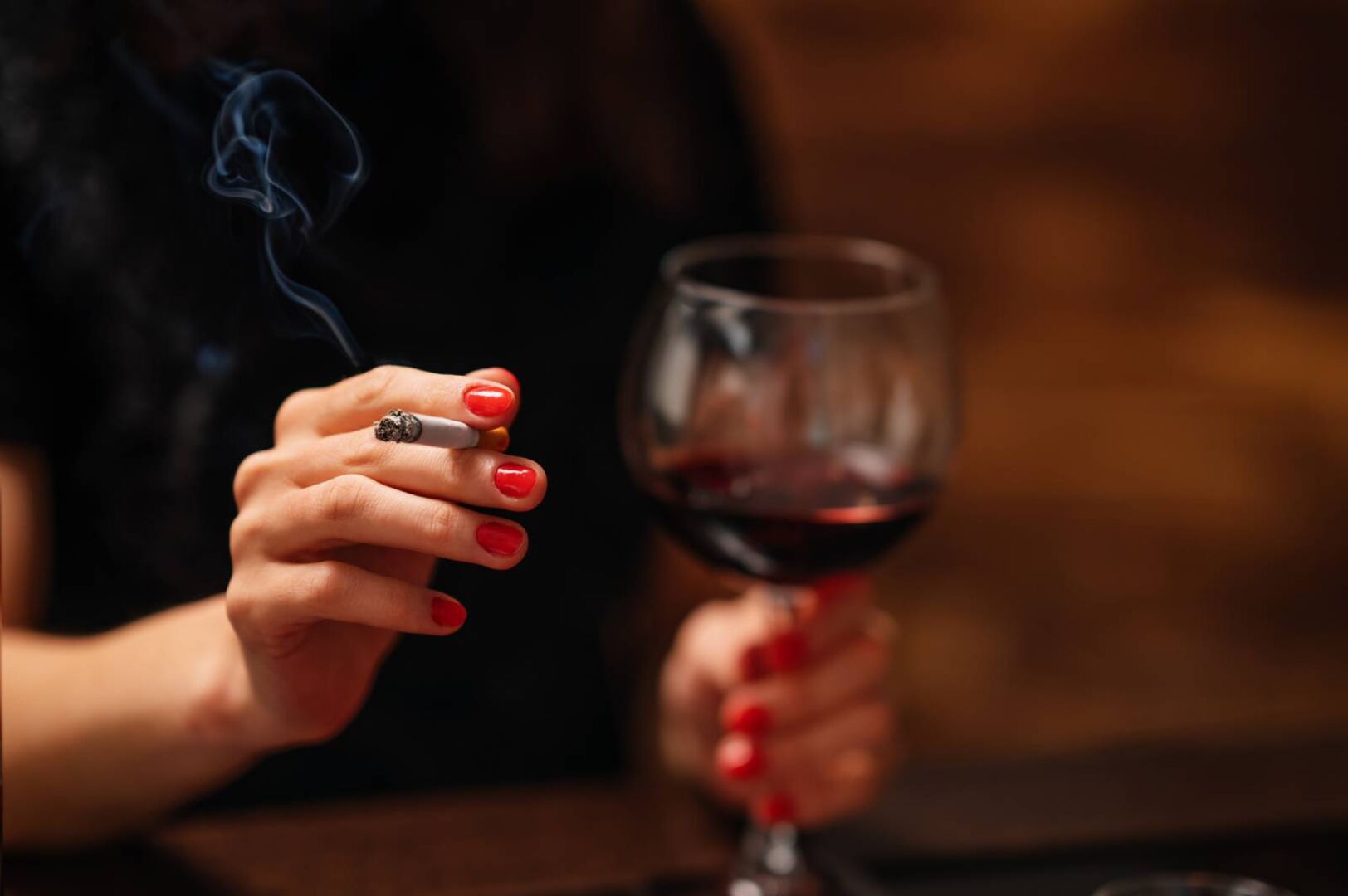 Junge Frau mit einer Zigarette in der einen und einem Glas Rotwein in der anderen Hand | Credit: iStock.com/SonerCdem