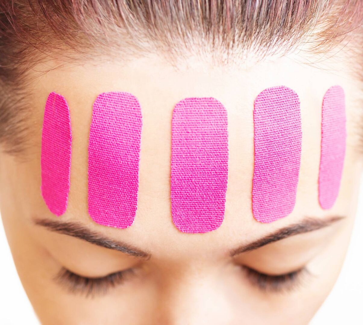 Junge Frau mit pinkfarbenen Beauty Tapes auf der Stirn | Credit: iStock.com/Remains