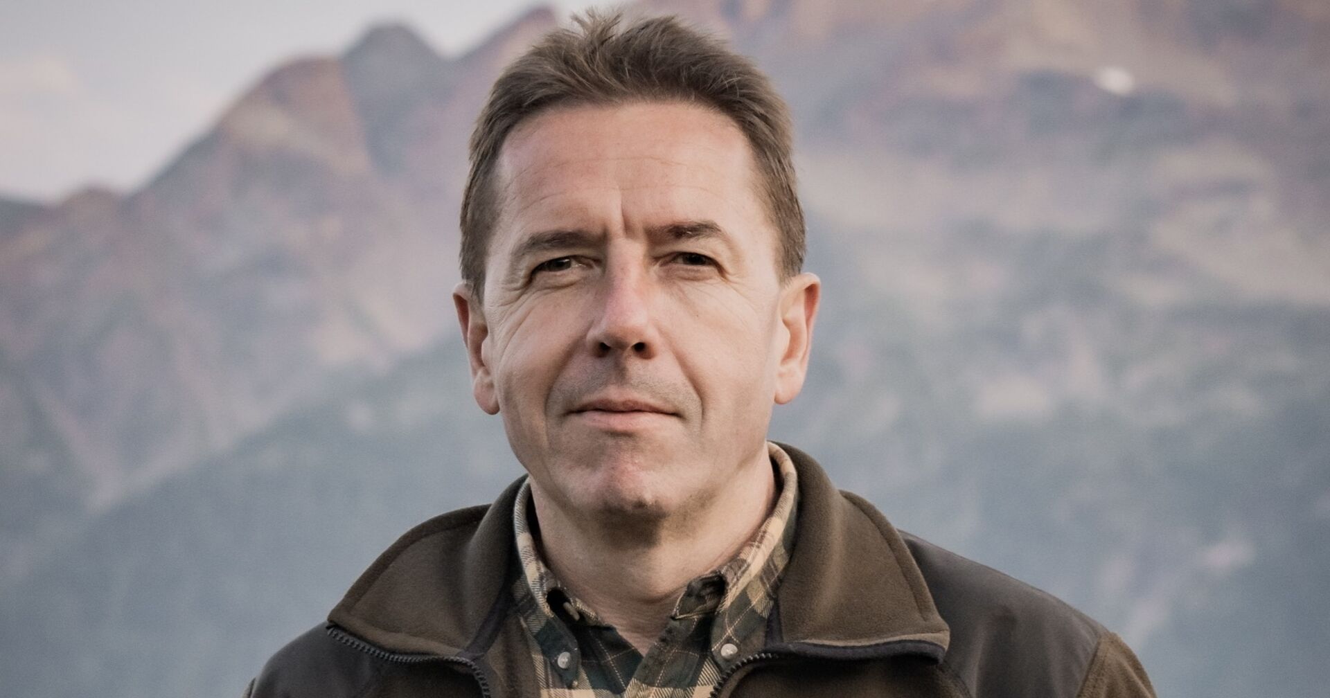 Erwin Angerer, der in Outdoor-Kleidung vor einem Gebirgsmassiv steht.