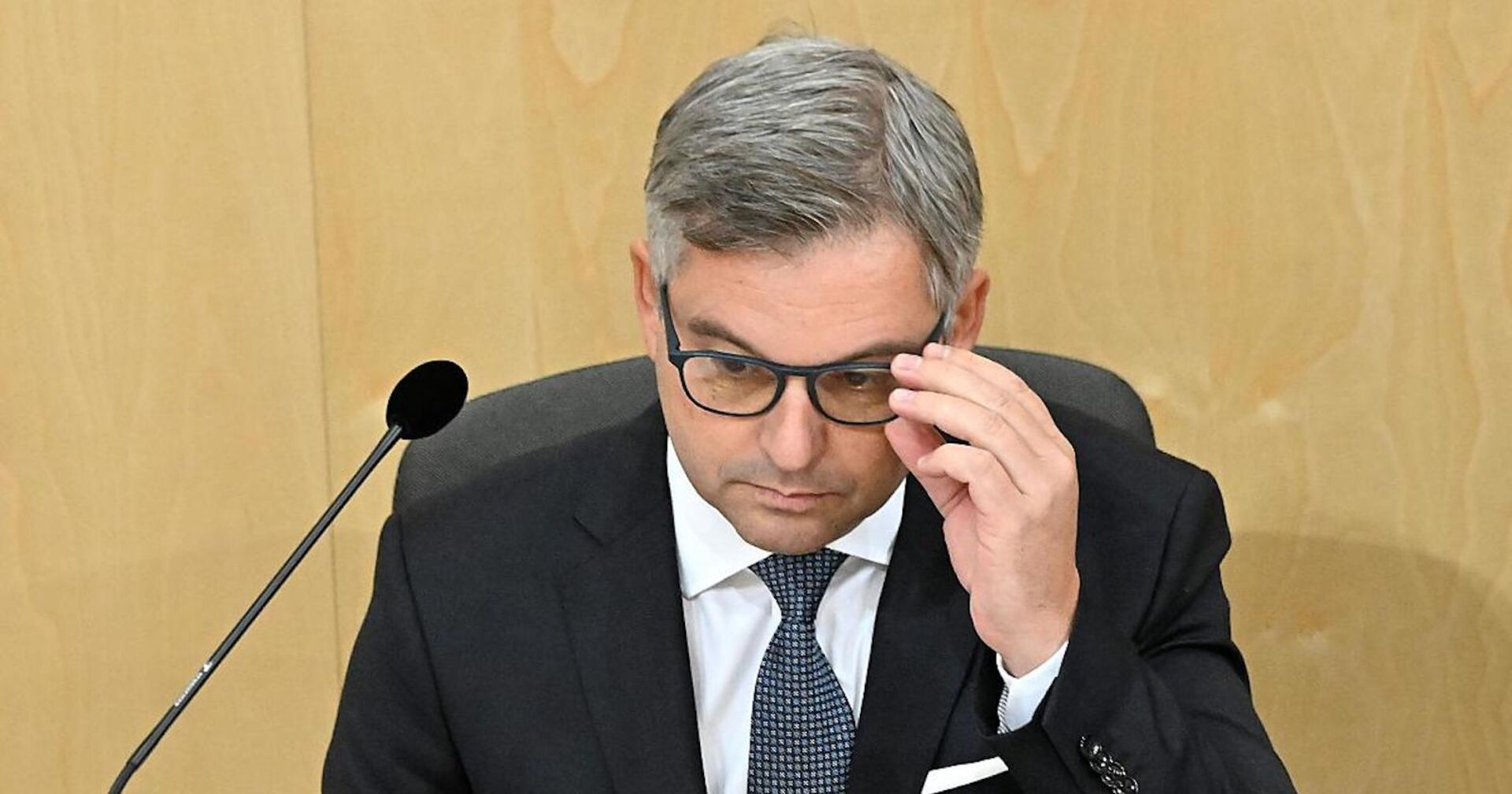 Porträt mit Mikrofon, greift sich an die Brille