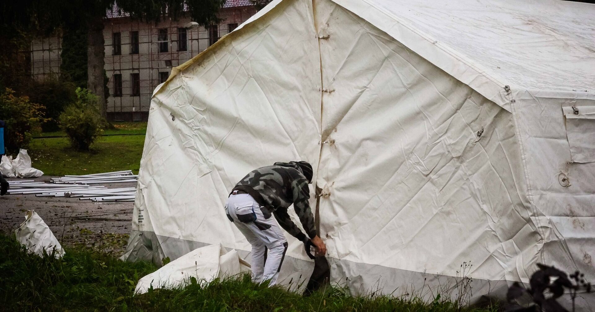 Ein Mann öffnet ein weißes, schmutziges Zelt an einem Regentag.