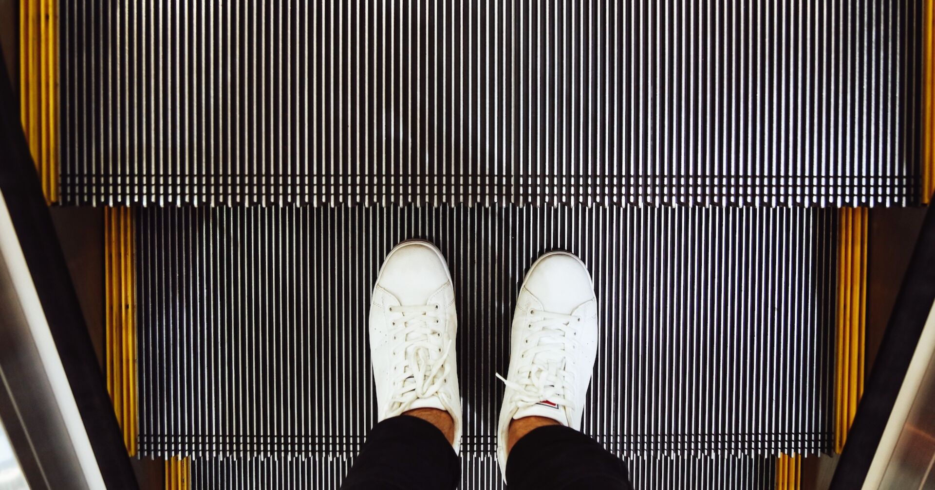 Mann mit weißen Schuhen auf einer Rolltreppe | Credit: iStock.com/toncd32