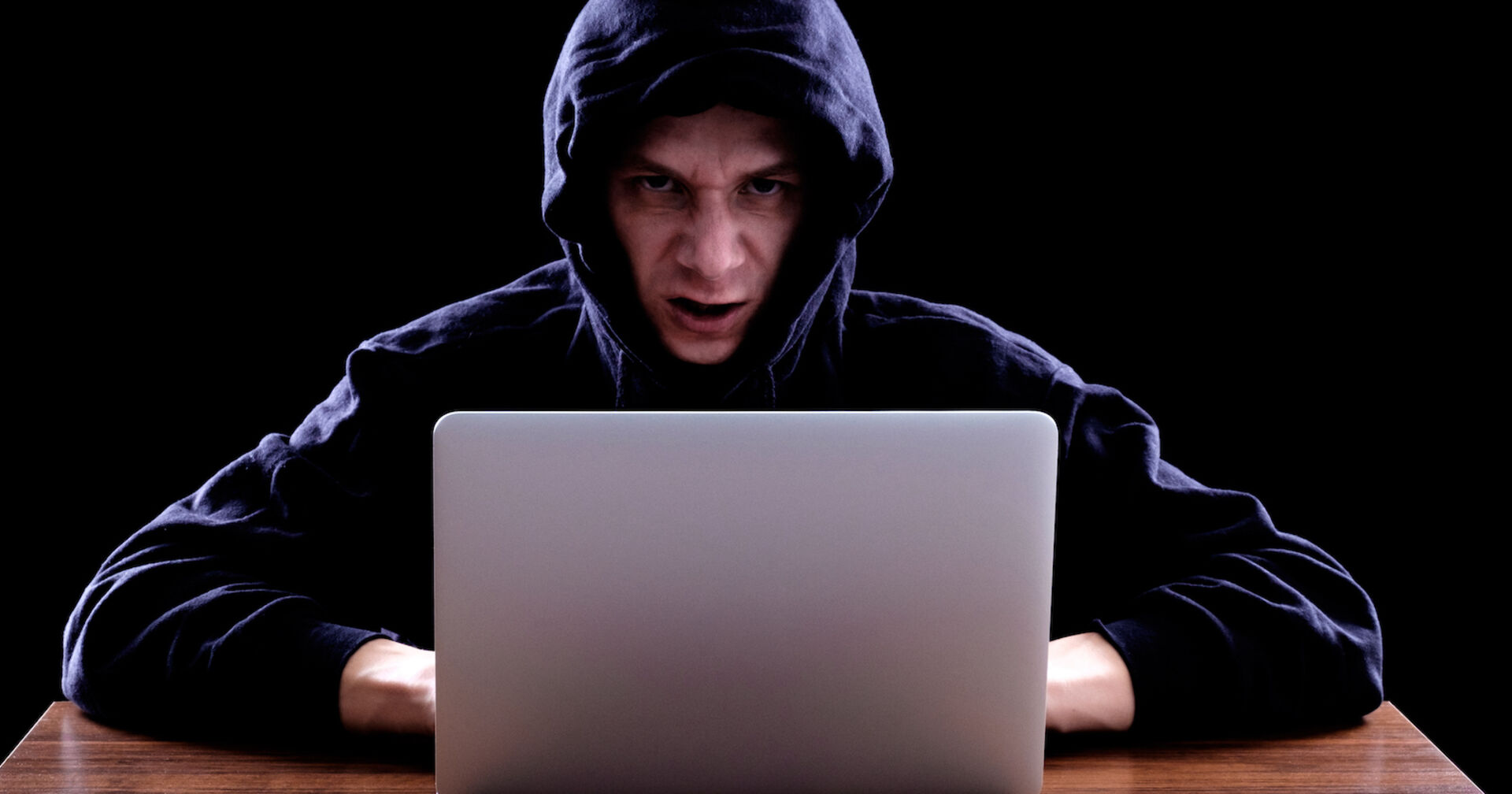 Mann mit schwarzem Kapuzenpullover vor einem Laptop| Credit: iStock.com/filistimlyanin