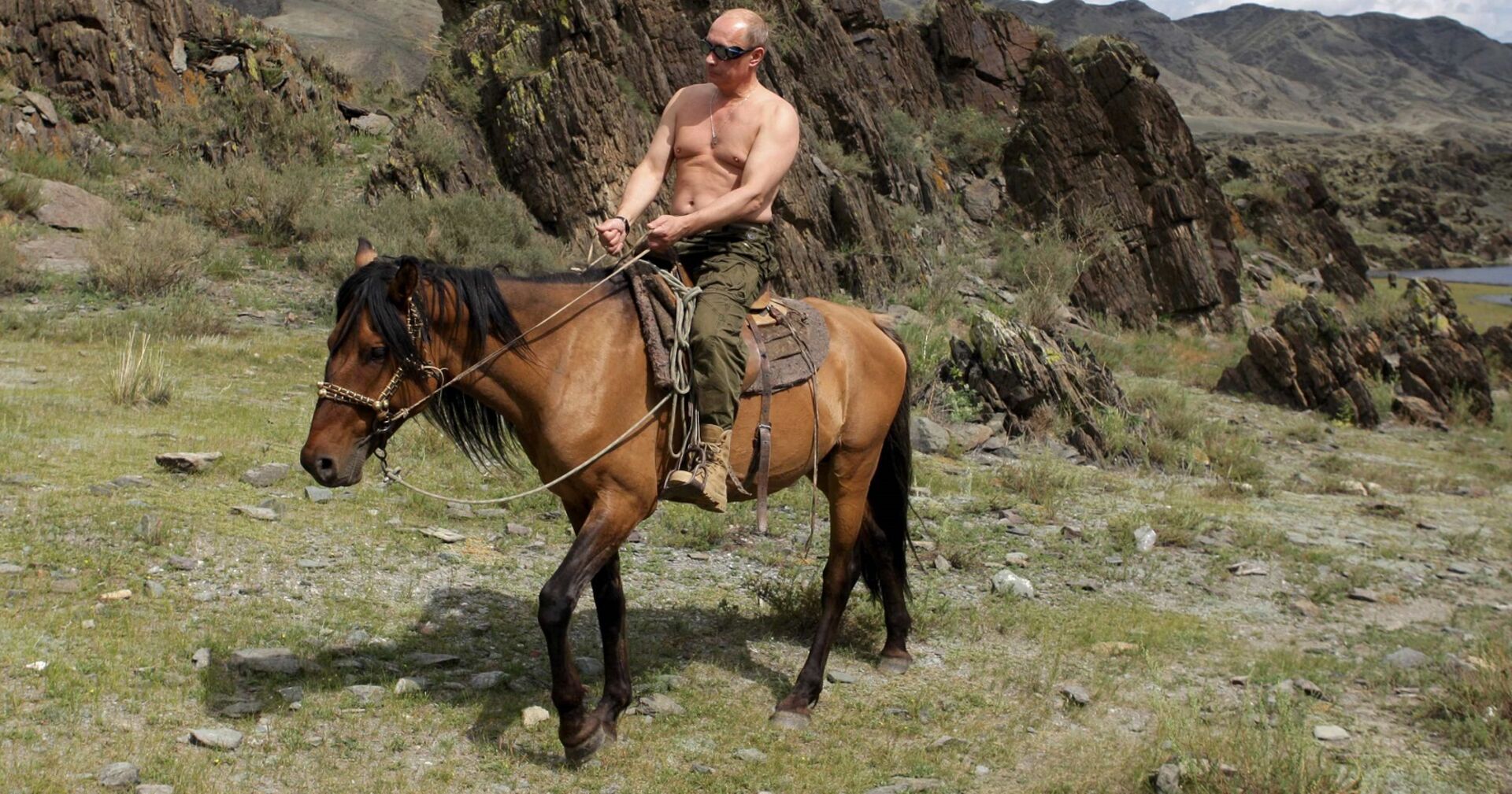 Putin mit nackten Oberkörper auf einem Pferd in den Bergen.
