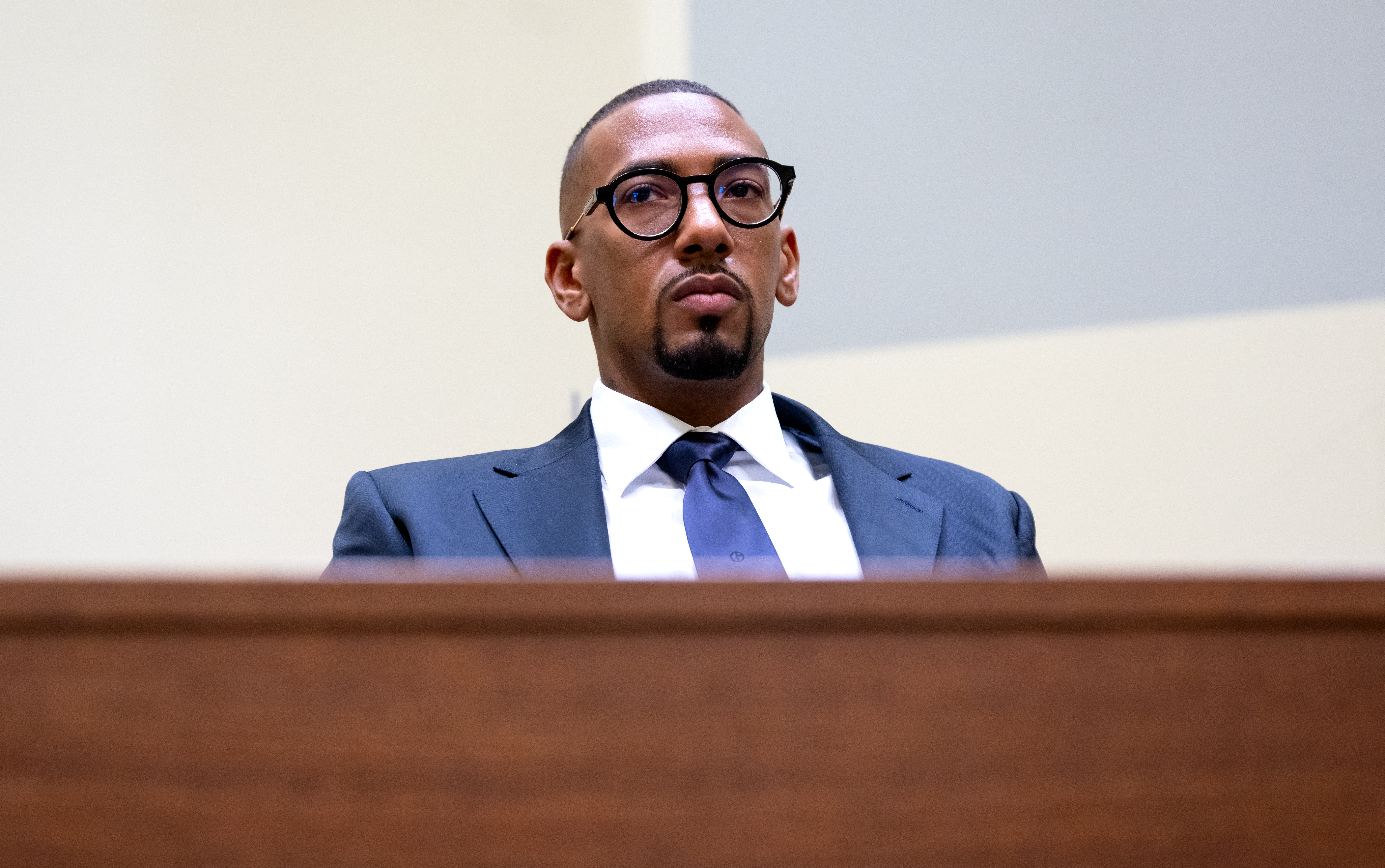 Fußballprofi Jerome Boateng sitzt, in einen eleganten Anzug gekleidet, auf der Anklagebank eines Gerichtssaals