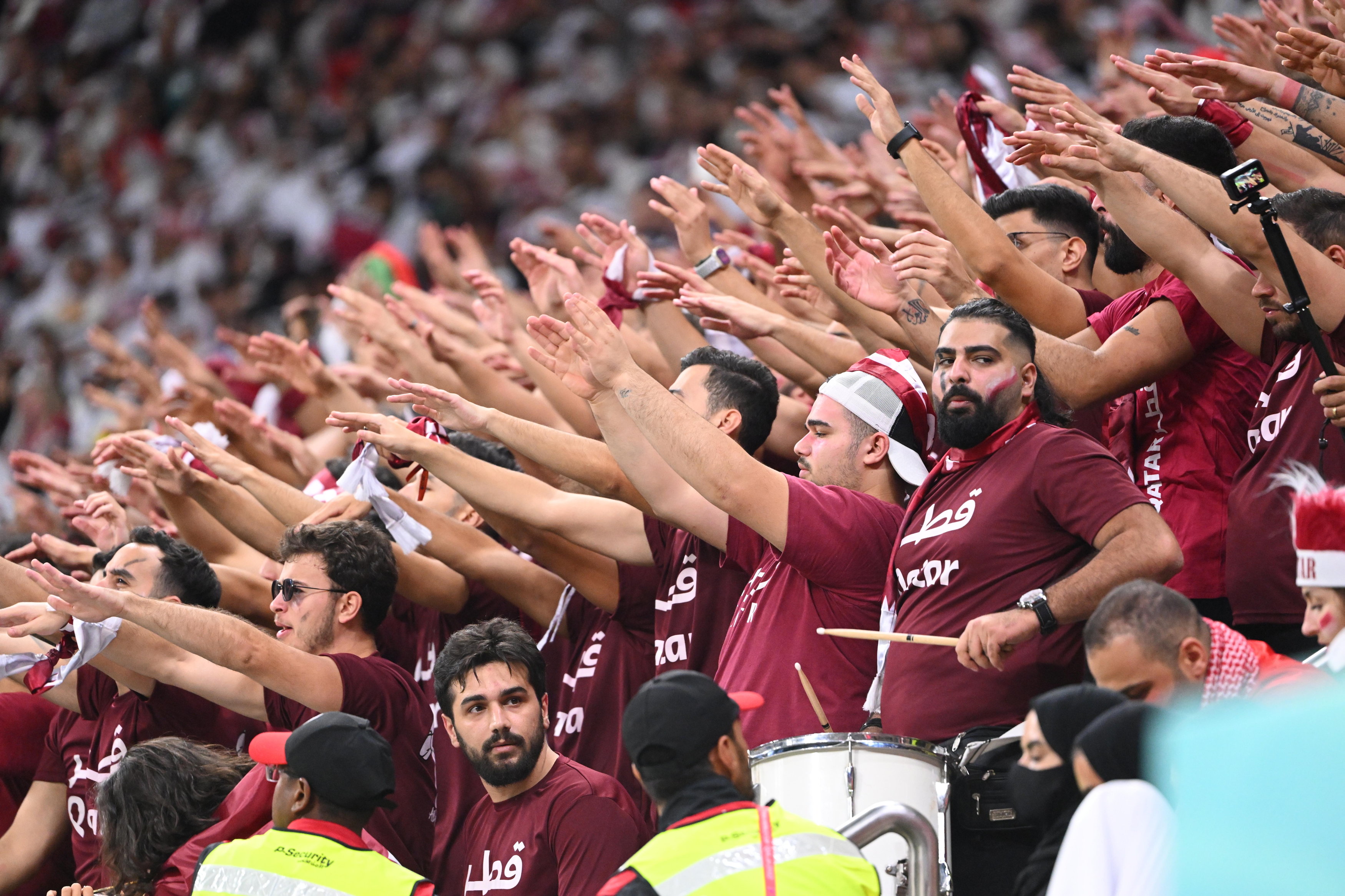 Eine Gruppe katarischer Fußballfans in roten T-Shirts, die koordiniert die Hände zum Jubeln heben