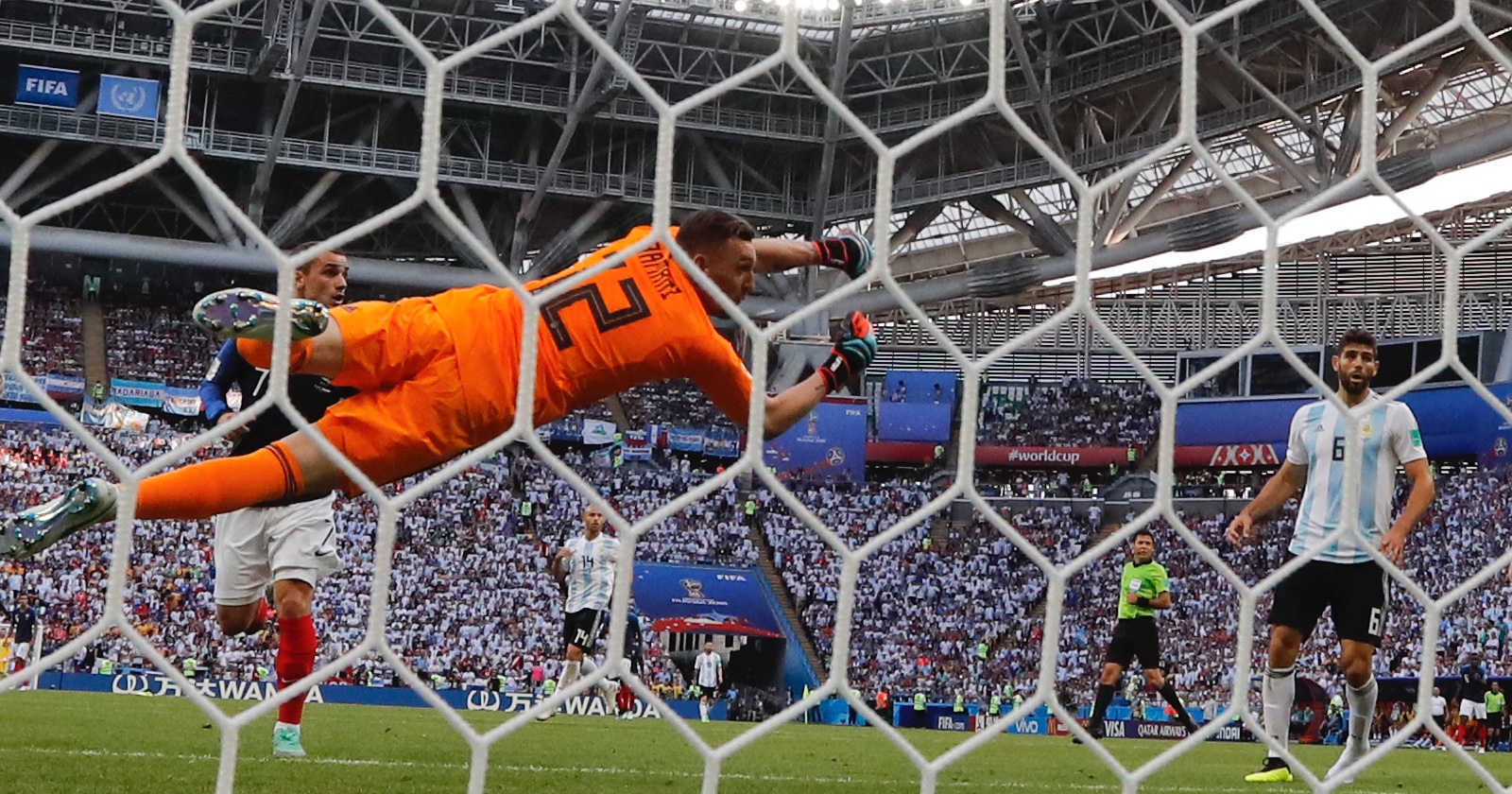 Der argentinische Fußball-Torhüter in einem orangen Dress, der - durch die Maschen des Tornetzes fotografiert -, durch die Luft hechtet