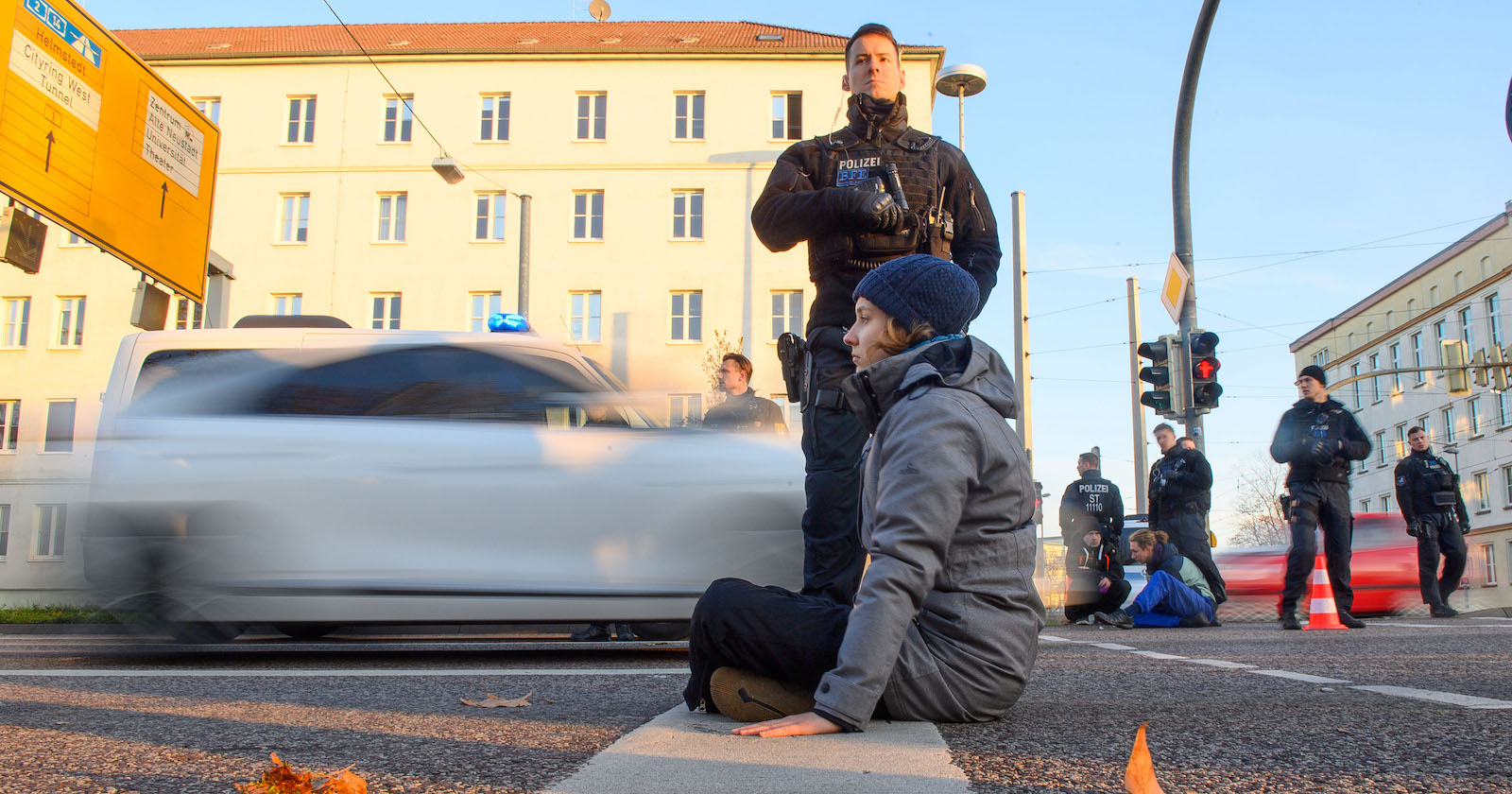 Junge Frau auf Fahrbahn sitzend, Polizist steht dahinter