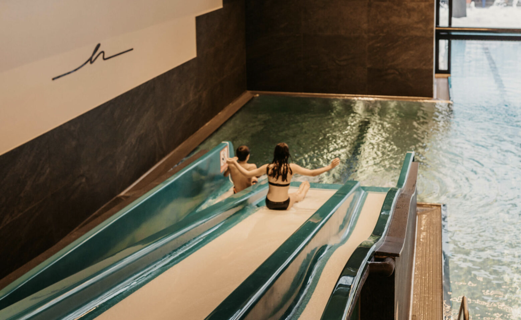 Zwei Kinder rutschen in den Indoorpool.