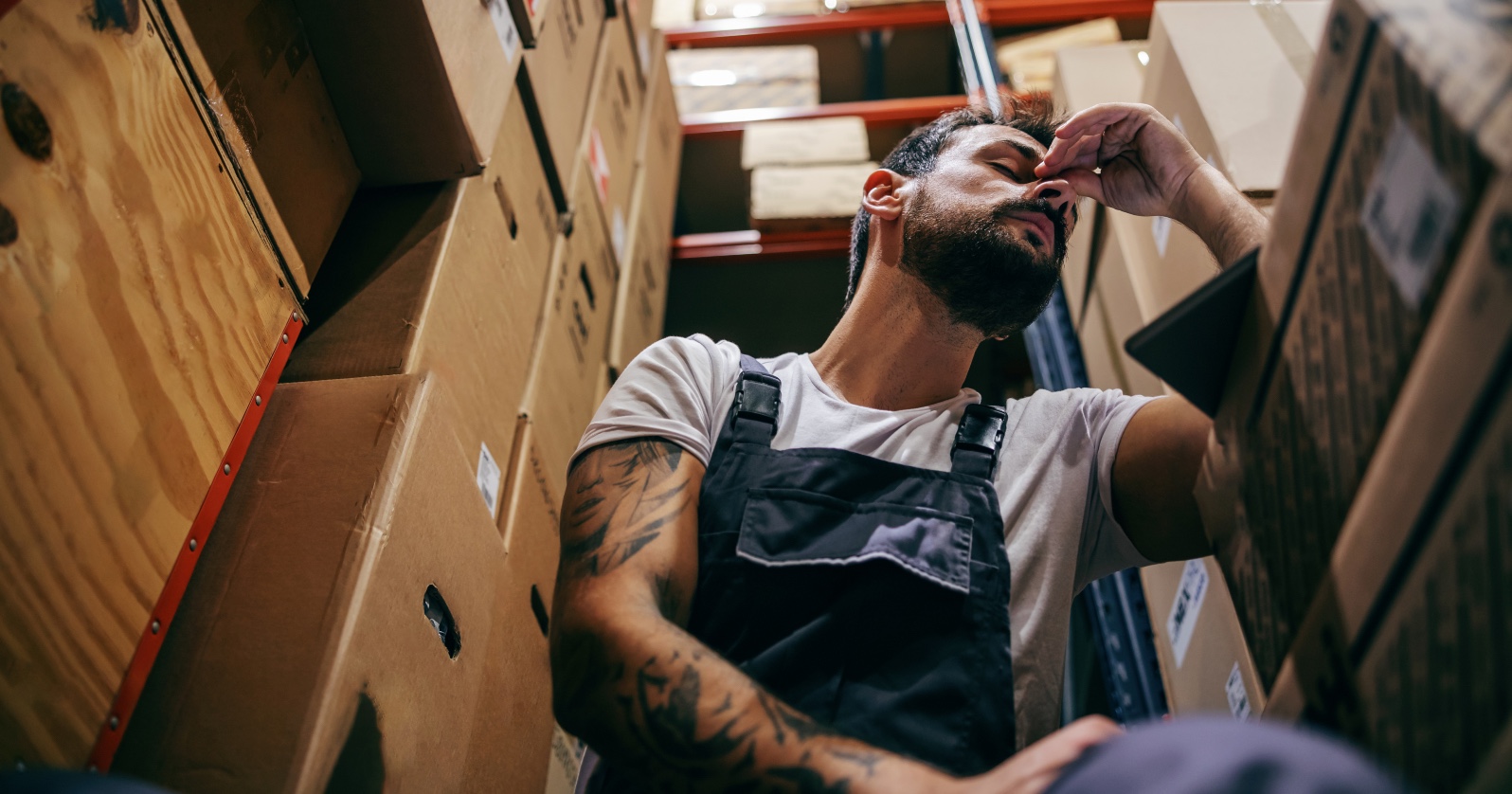 Erschöpfter, bärtiger Mann in einem Lagerraum. | Credit: iStock.com/dusanpetkovic