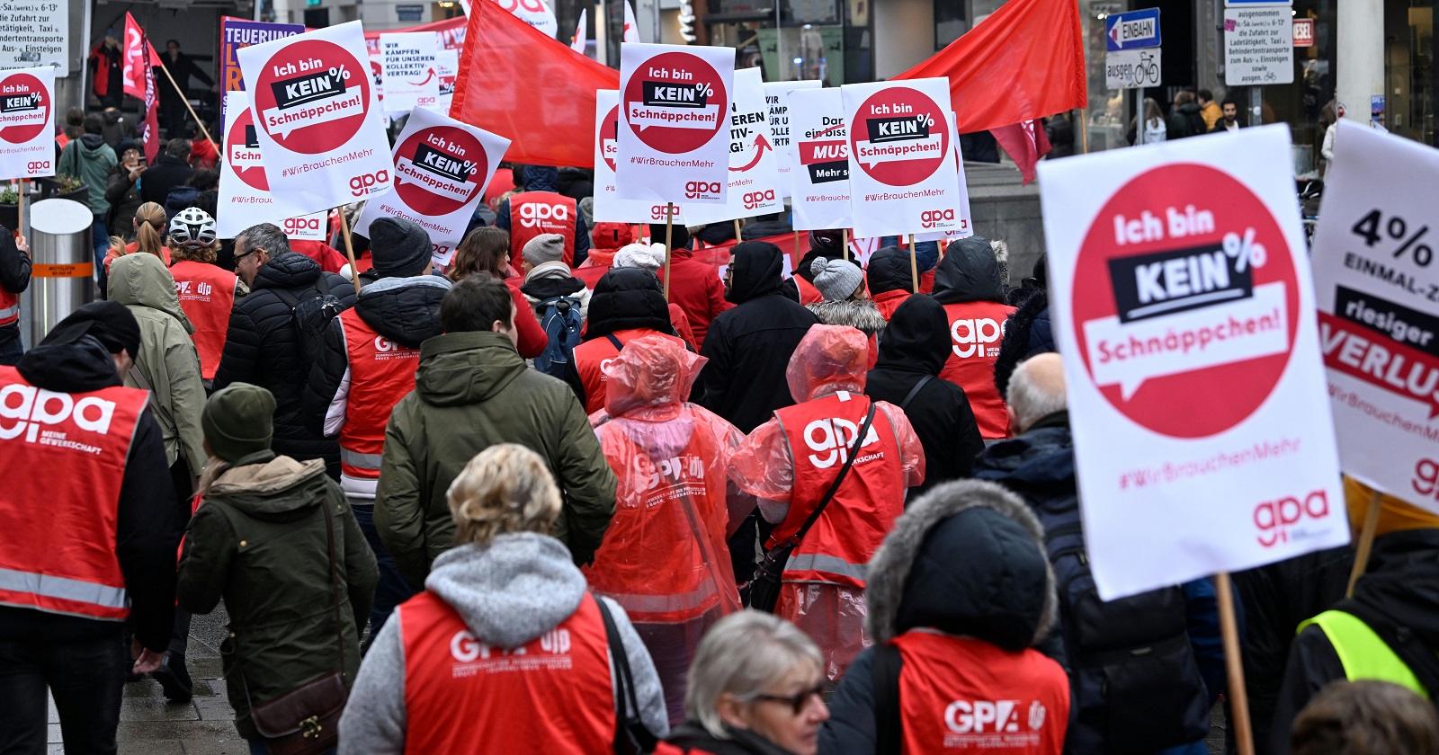 Menschen in roten Westen mit der Aufschrift &quot;GPA&quot; demonstrieren mit Plakaten für ein höheres Gehalt.