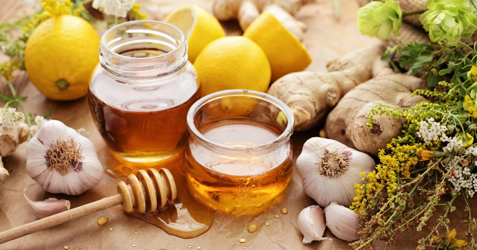 Zwei offene Gläser Honig, umgeben von Zitronen und Ingwer | Credit: iStock.com/KMNPhoto