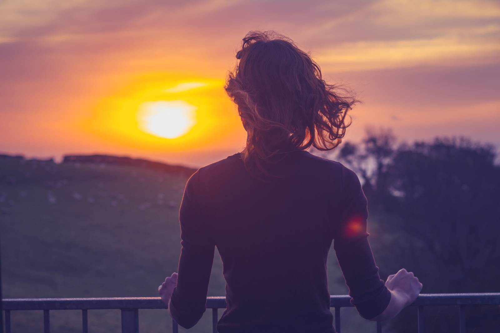 Junge Frau beobachtet vom Balkon aus den Sonnenuntergang | Credit: iStock.com/lolostock