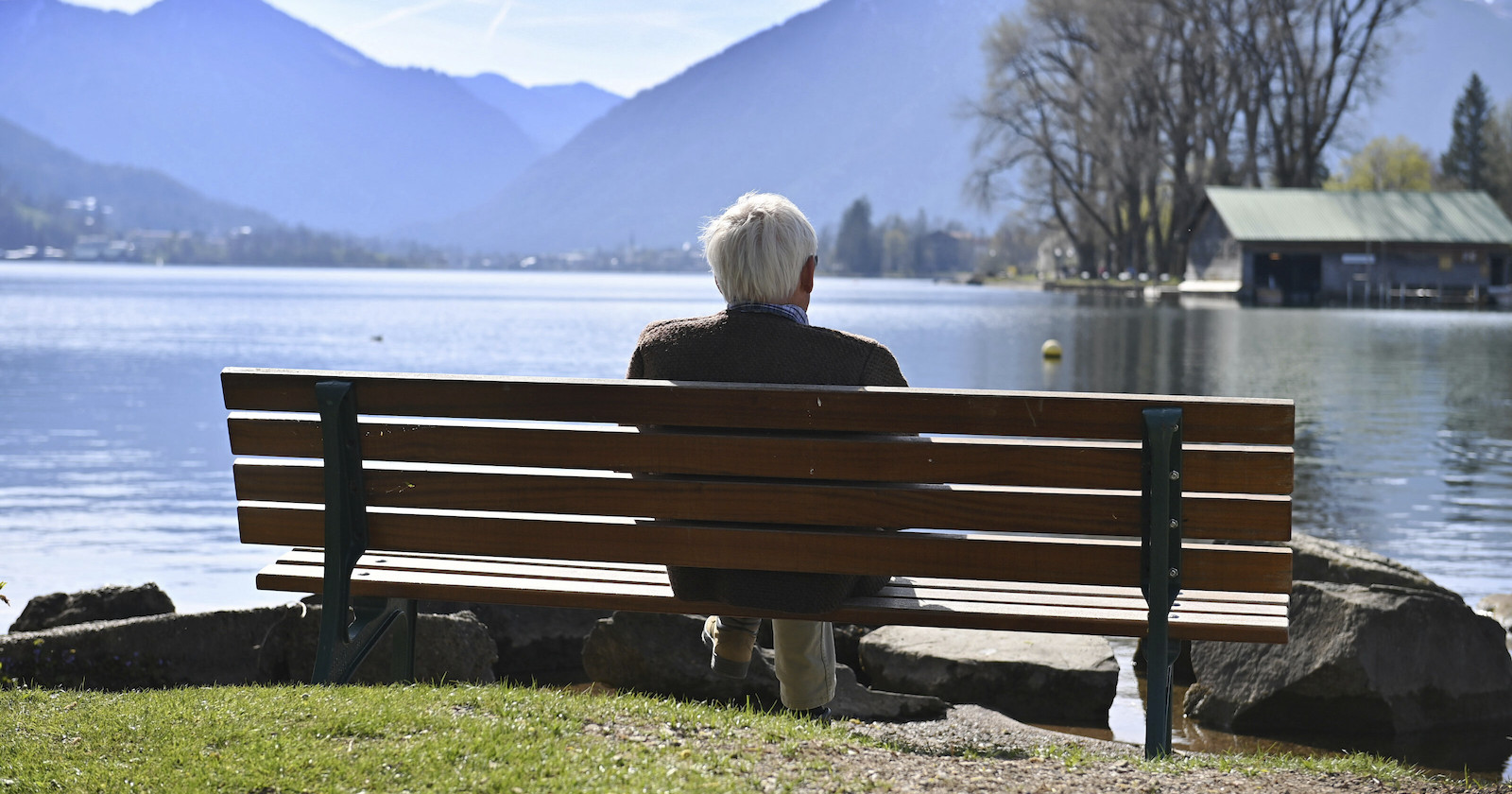 Mann sitzt auf Parkbank mit Blick auf See