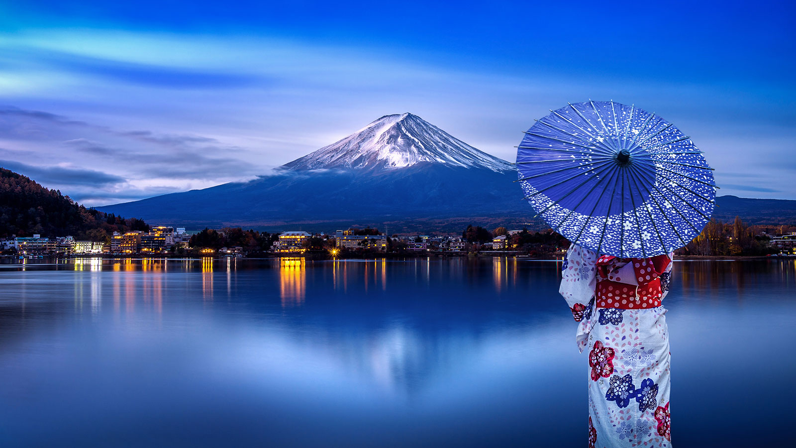 Japanerin im Kimono und mit Regenschirm am Ufer eines Sees mit Blick auf den Fuji | Credit: iStock.com/tawatchaiprakobkit