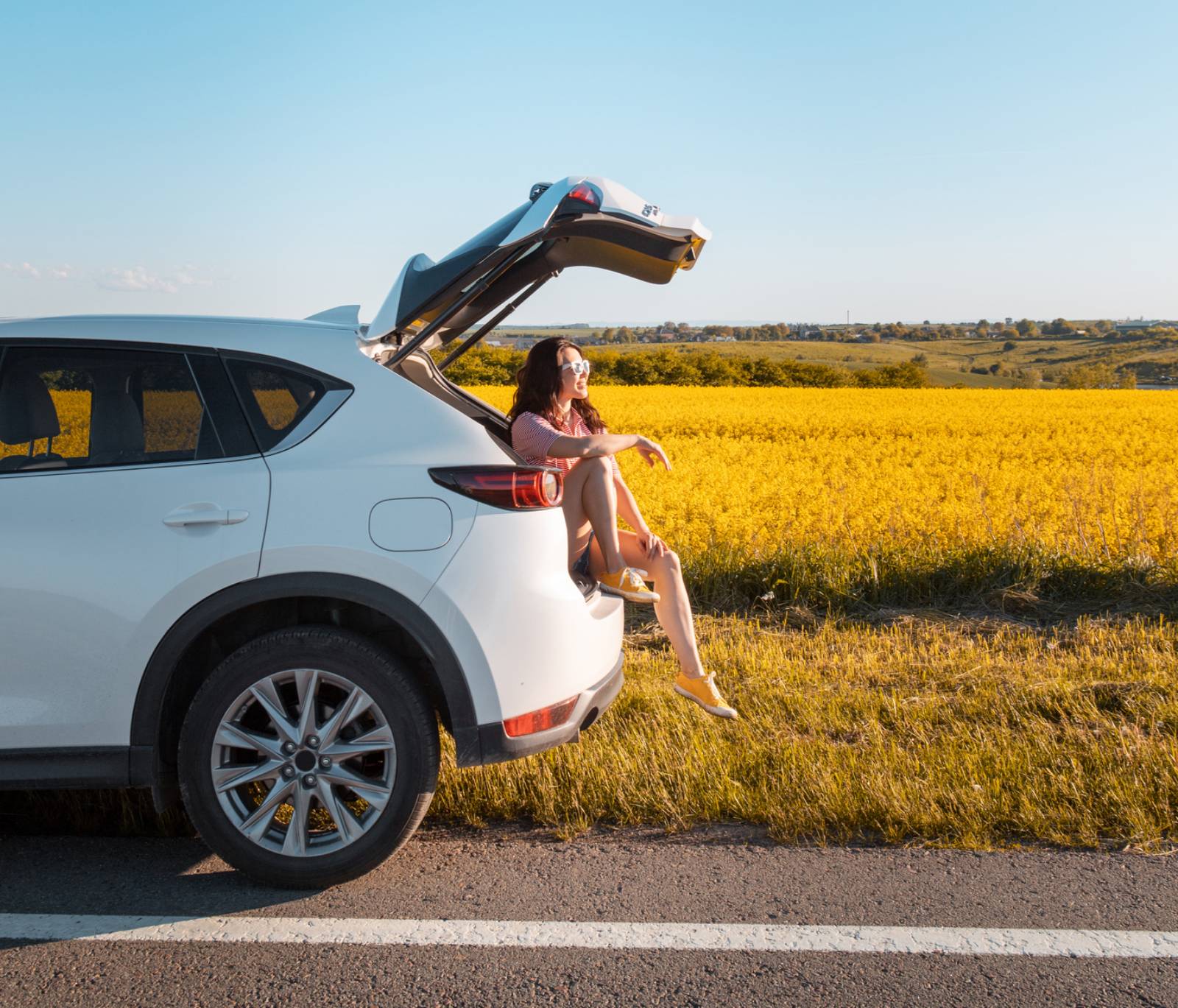 Frau sitzt im aufgeklappten Kofferraum ihres SUV und genießt die Sonne | Credit: iStock.com/Vera_Petrunina