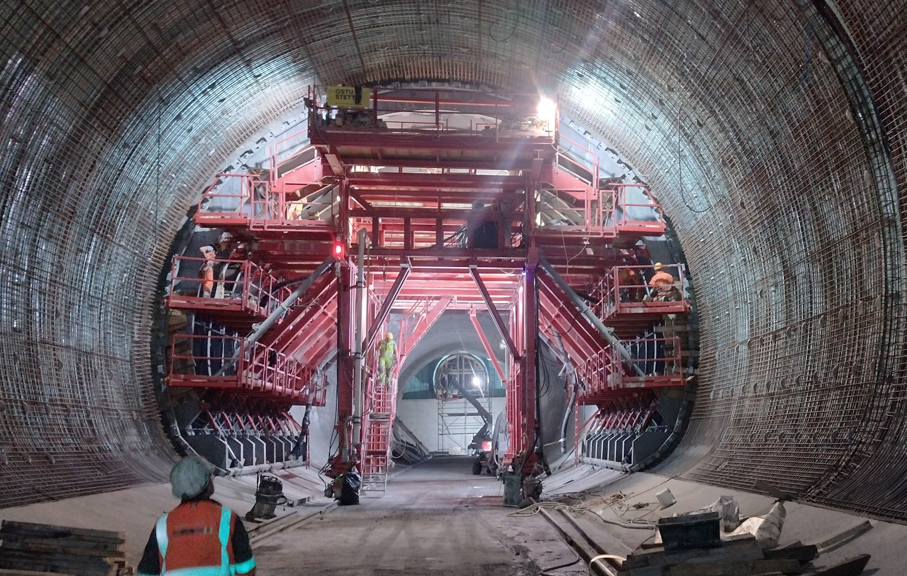 Arbeiter, die im Inneren eines Kraftwerkes auf einem überdimensional großen, roten Baugerüst ihrer Arbeit nachgehen