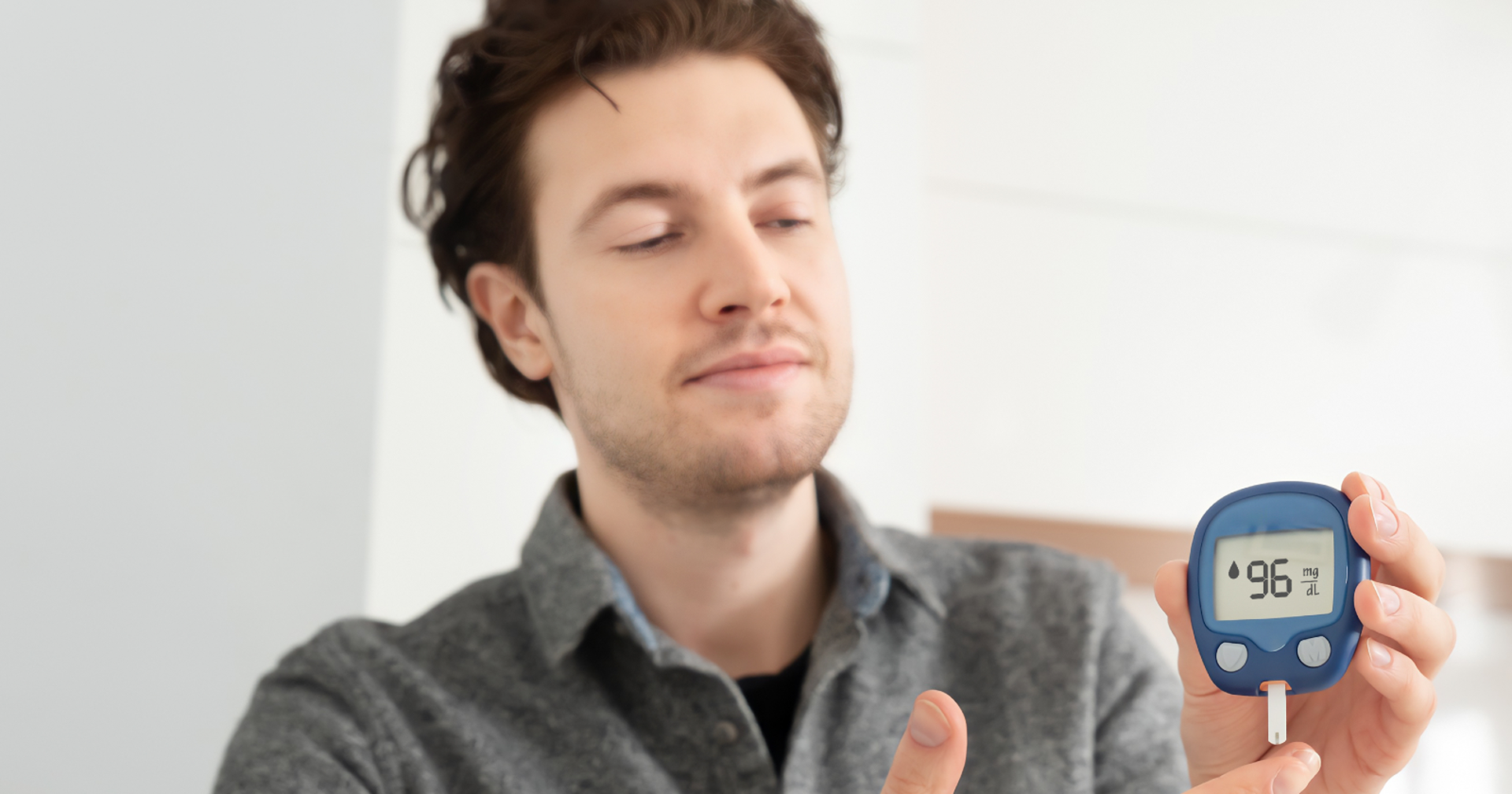 Ein junger Mann mit braunen Haaren hält ein Blutzuckermessgerät in seinen Händen
