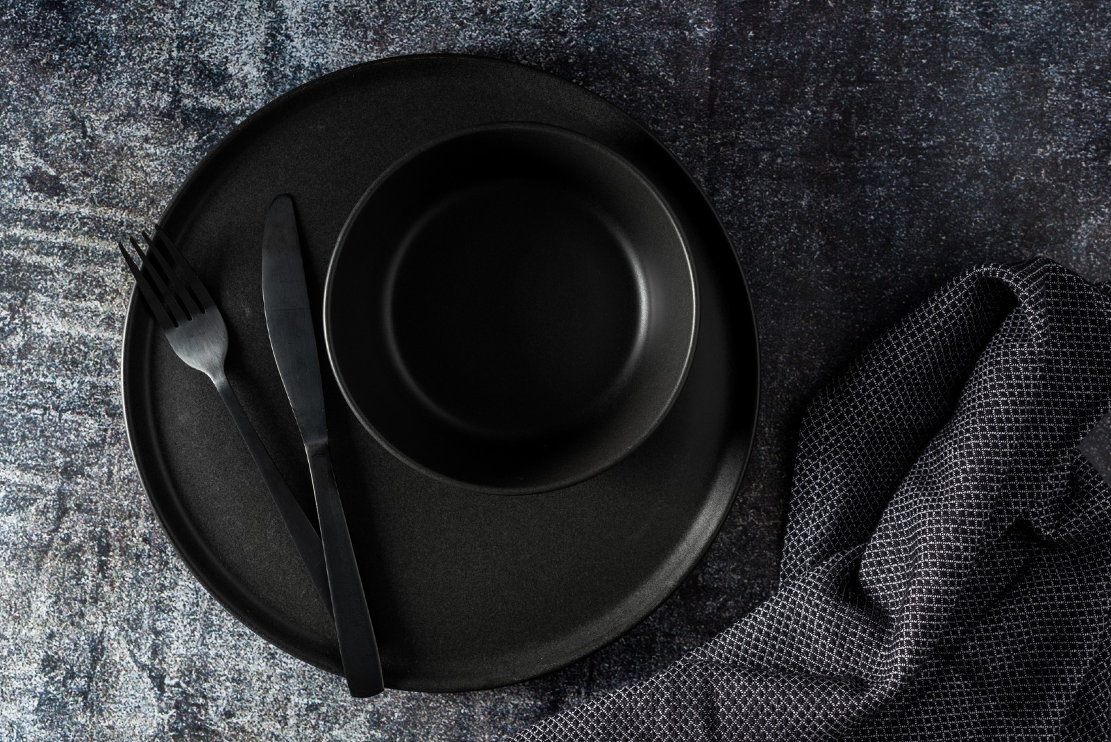 Schwarzer Teller mit schwarzem Besteck liegt auf einem schwarzen Tisch | Credit: iStock.com/Stockphoto24