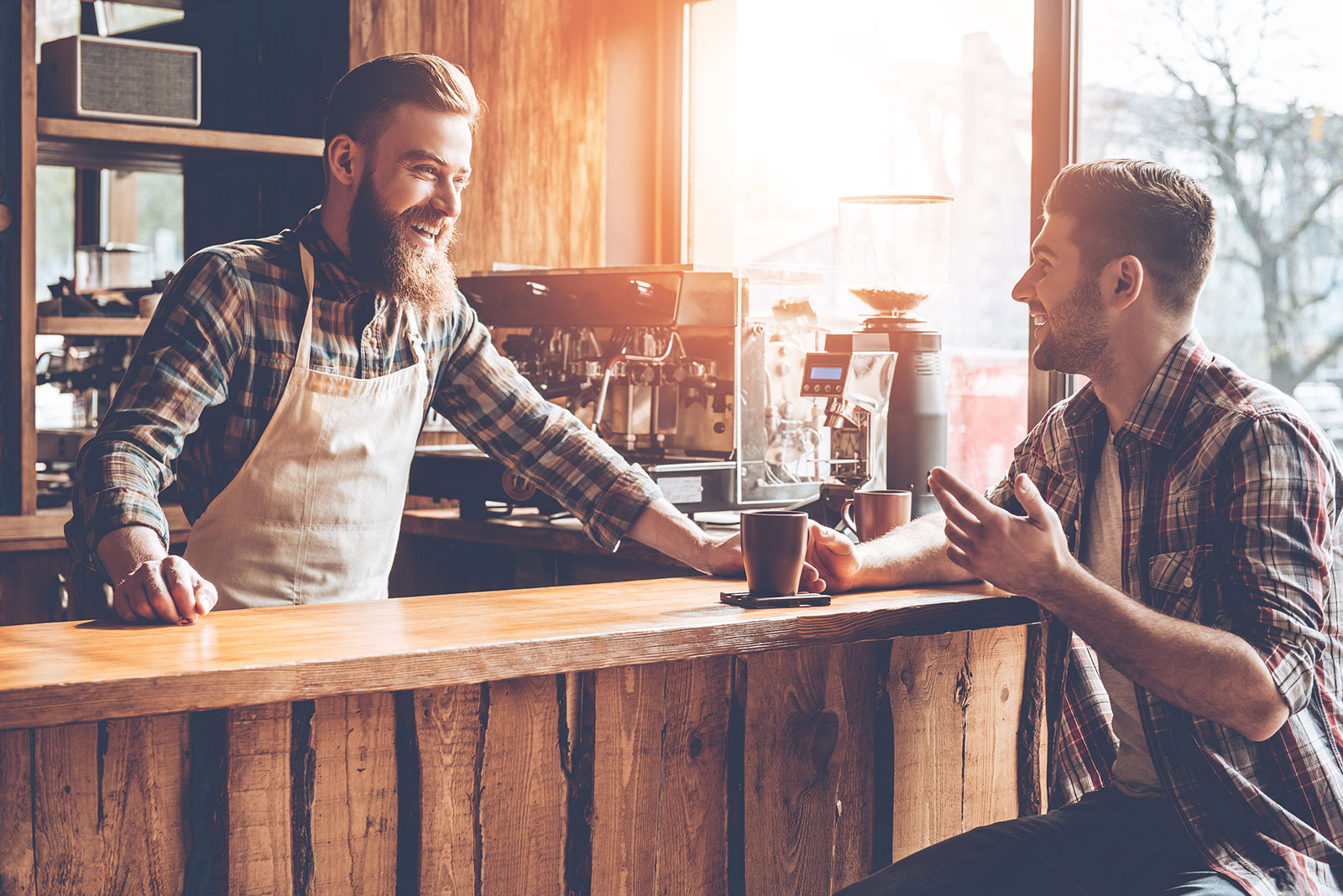 Barista hinter der Theke im Gespräch mit einem Kunden | Credit: iStock.com/g-stockstudio