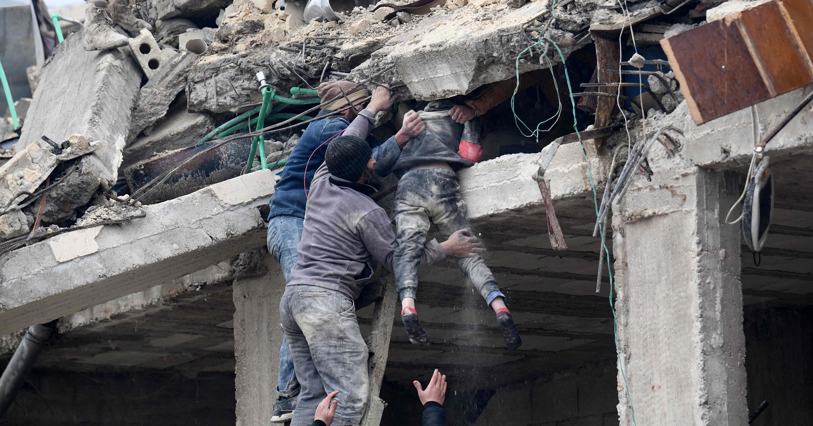 Drei Männer ziehen ein verletztes Mädchen aus den Trümmern eines Gebäudes.