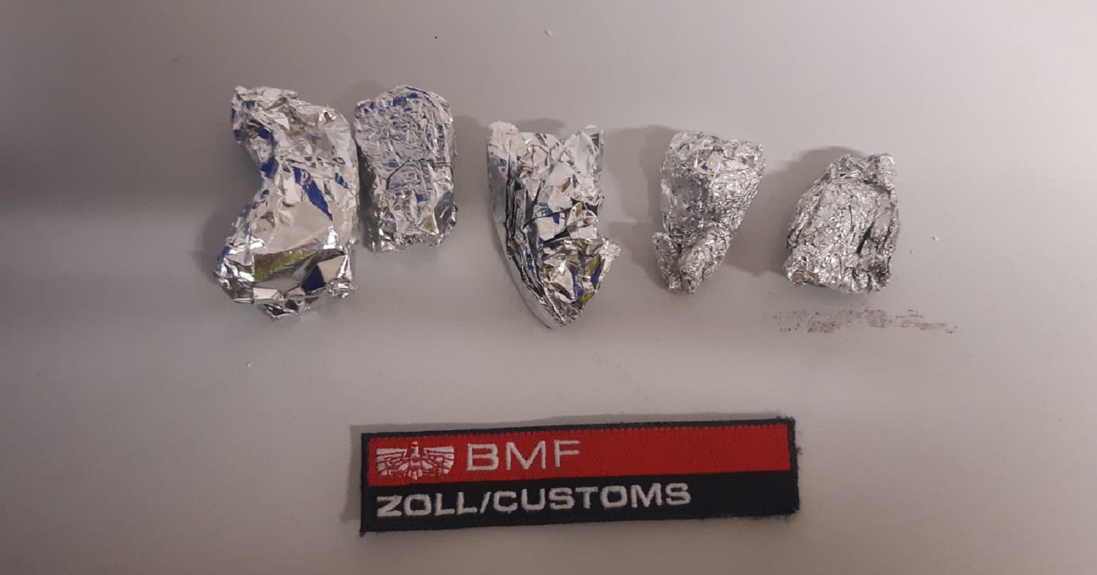Vier kleine Päckchen aus Aluminiumfolie, darunter ein Schild mit der Beschriftung &quot;BMF / Zoll / Customs&quot;