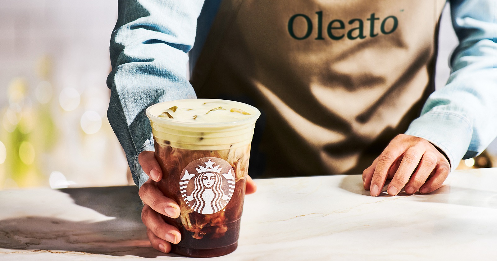 Eine Hand reicht einen Becher mit Oleato Golden Foam in einem Becher mit Starbucks Logo über den Tresen